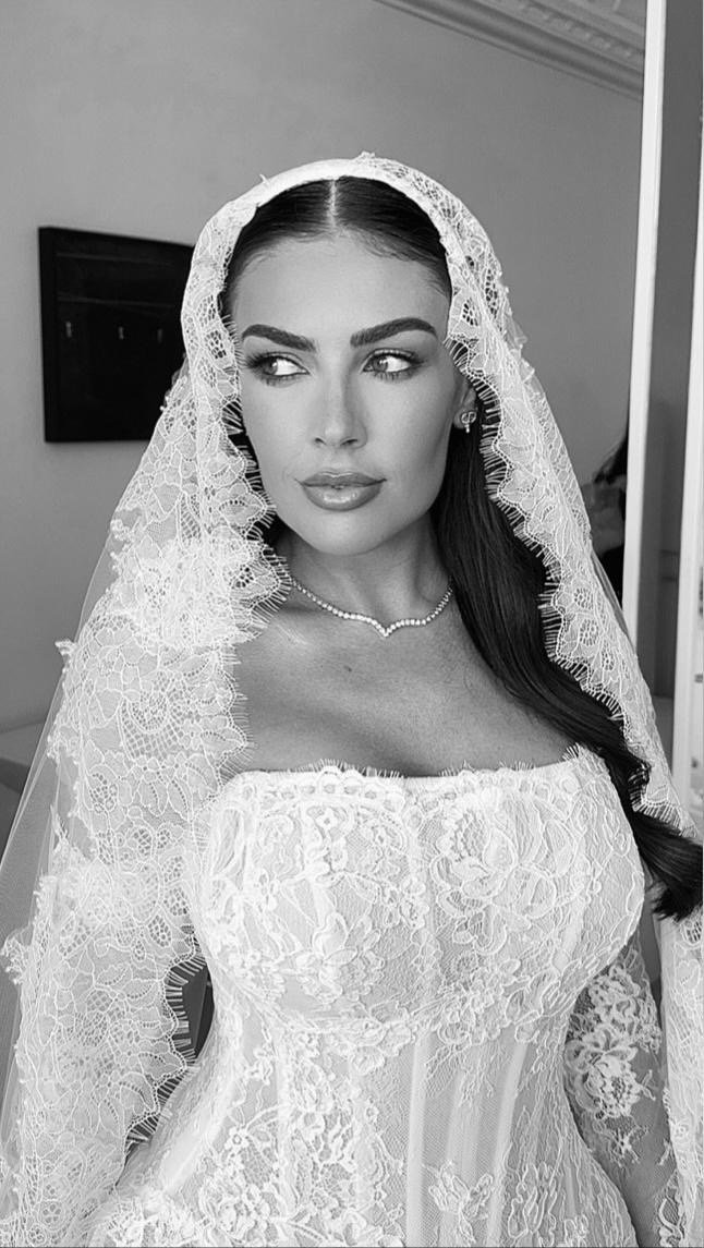 Black and white photo of a woman in a wedding dress with lace details and a headscarf, looking to the side.