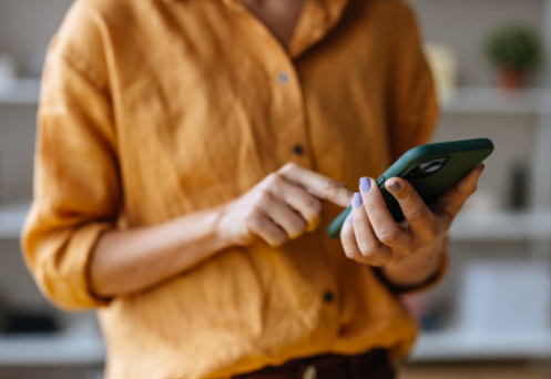 Person wearing a mustard yellow shirt using a smartphone.
