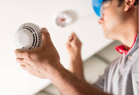 A person installing or replacing a smoke detector on the ceiling.