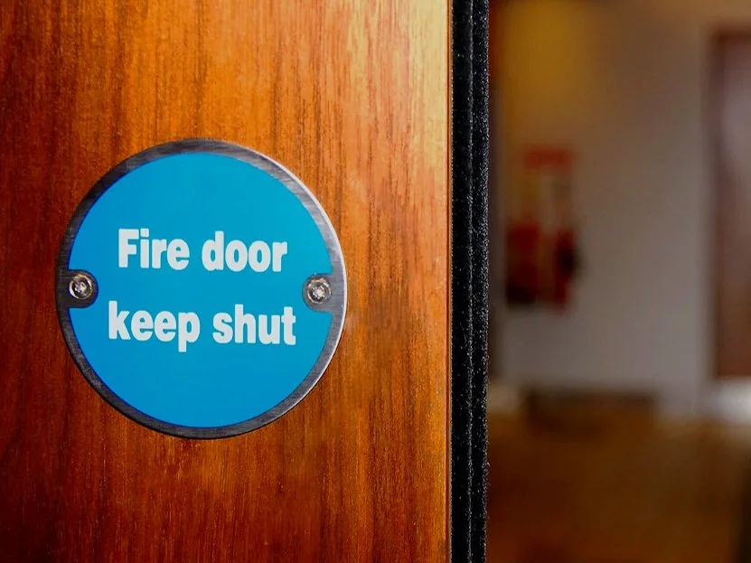 Blue circular sign on wooden door that reads "Fire door keep shut" in white letters.
