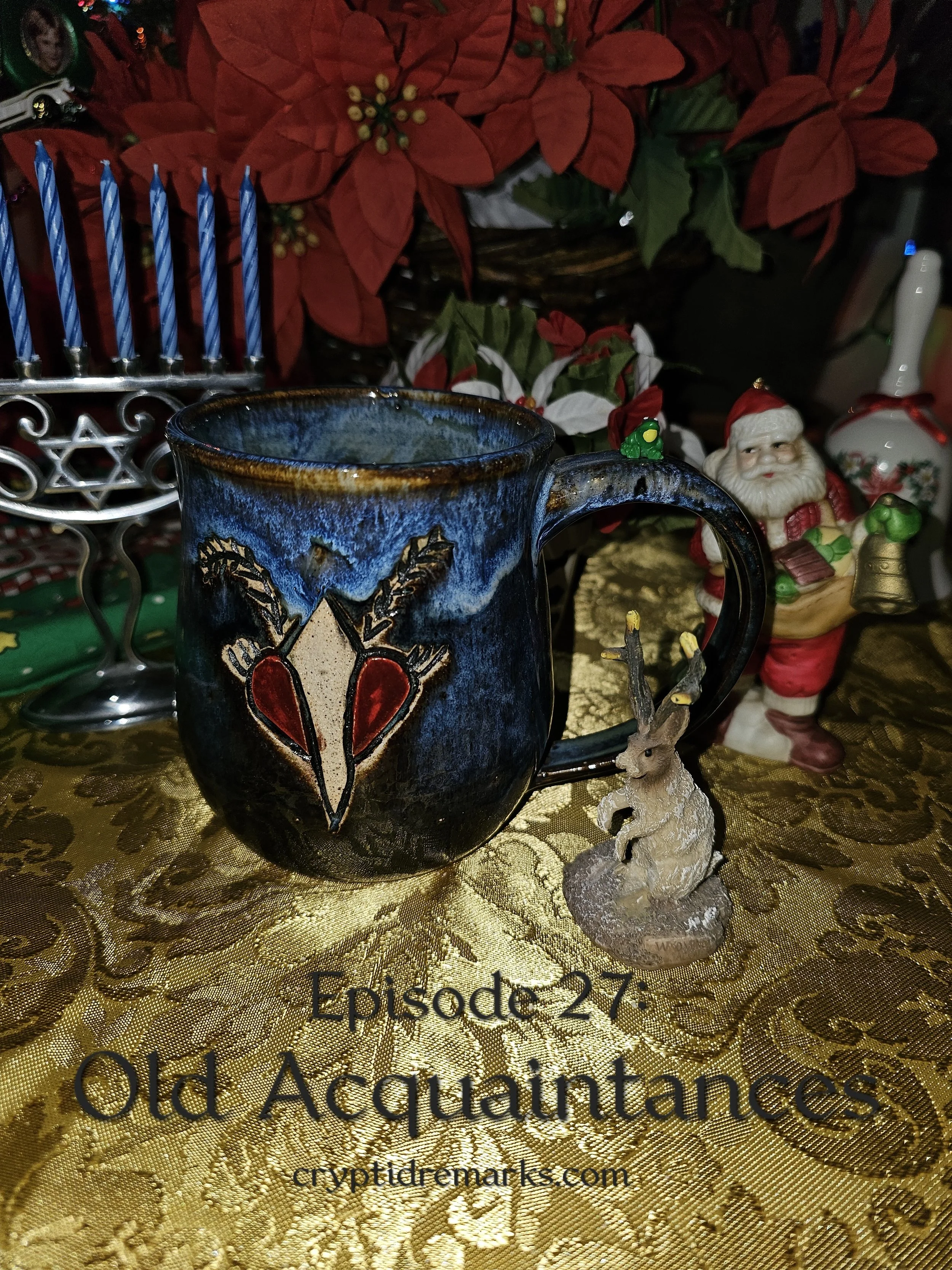 A mug with a Mothman decoration on a festive tablecloth with holiday symbols and ornaments nearby