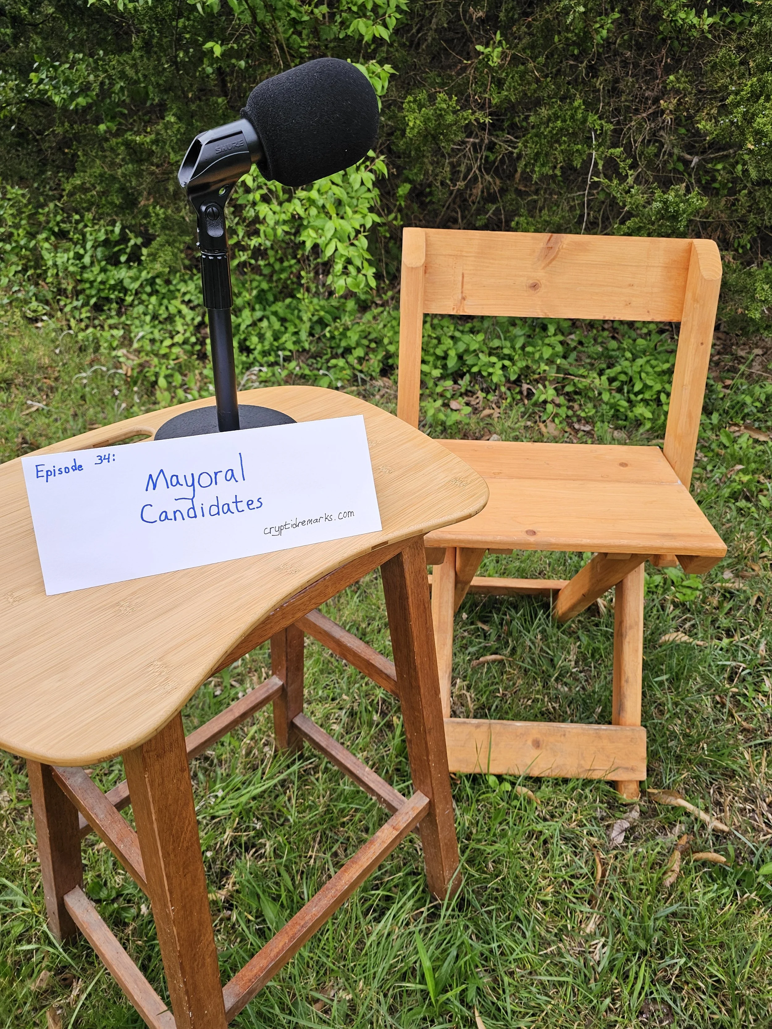 A folding wooden chair and small desk in a field, with a microphone and an envelope.