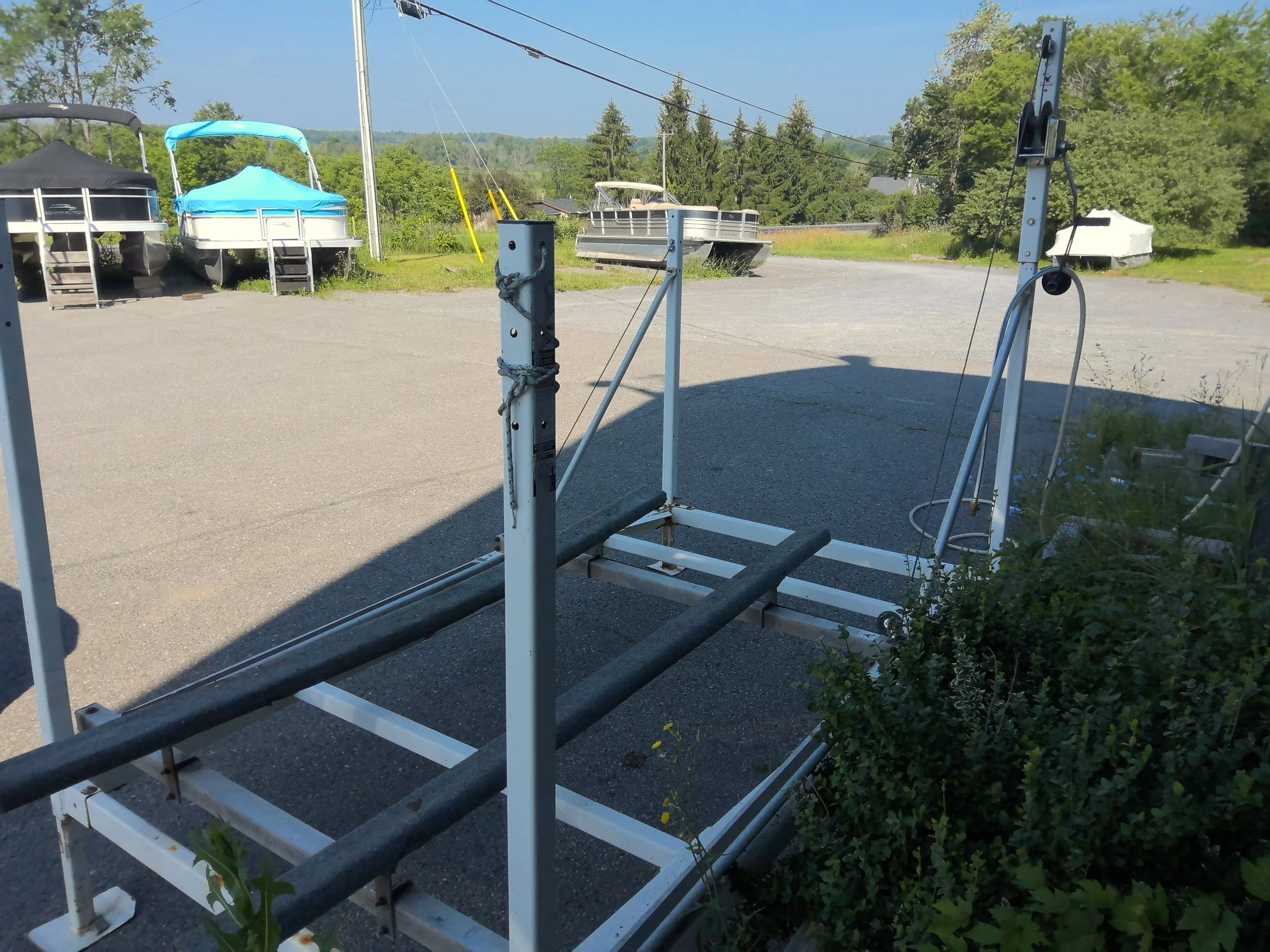 Empty boat lift with two boats on either side, some covered boats in the background, and a scenic view of trees and distant hills.
