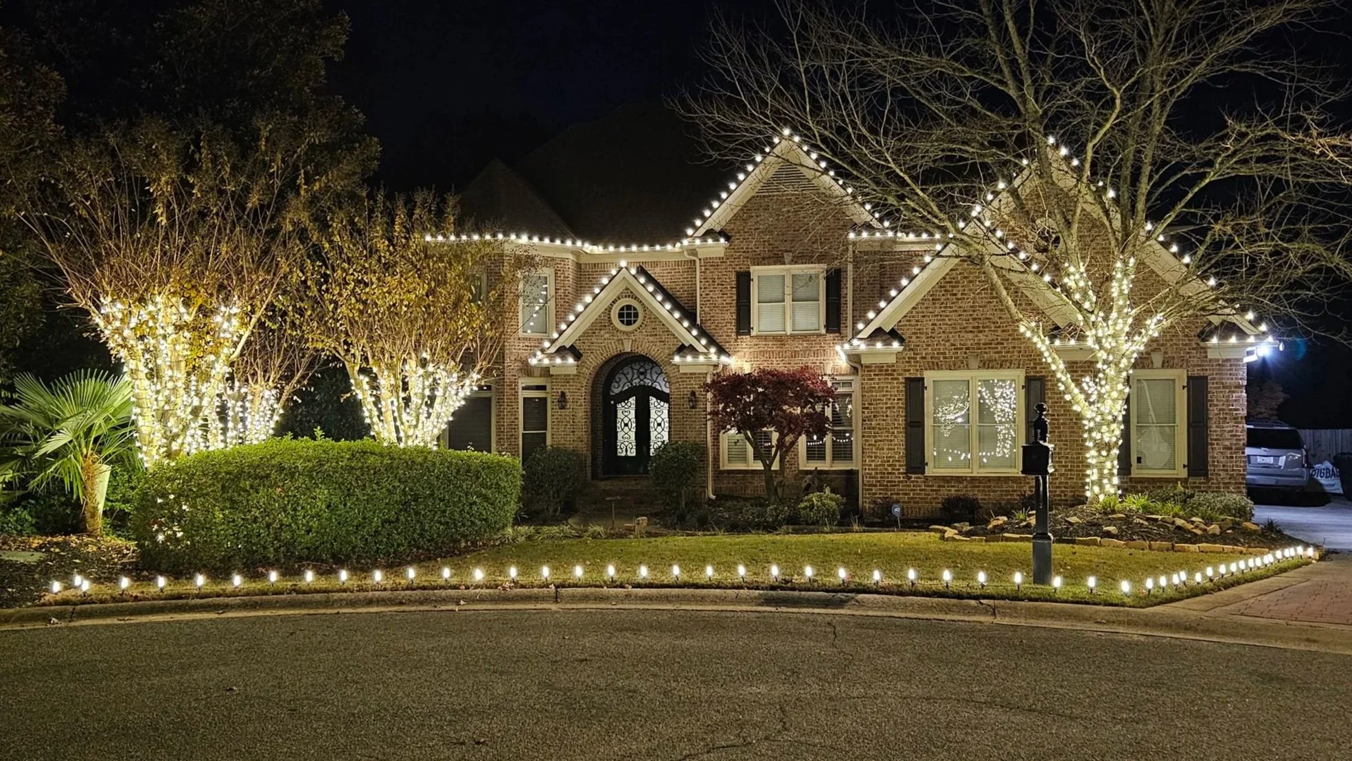 Warm white Christmas light installation featuring roofline pathway lighting and multiple tree wraps in Vinings Estates by Rich Lighting Co