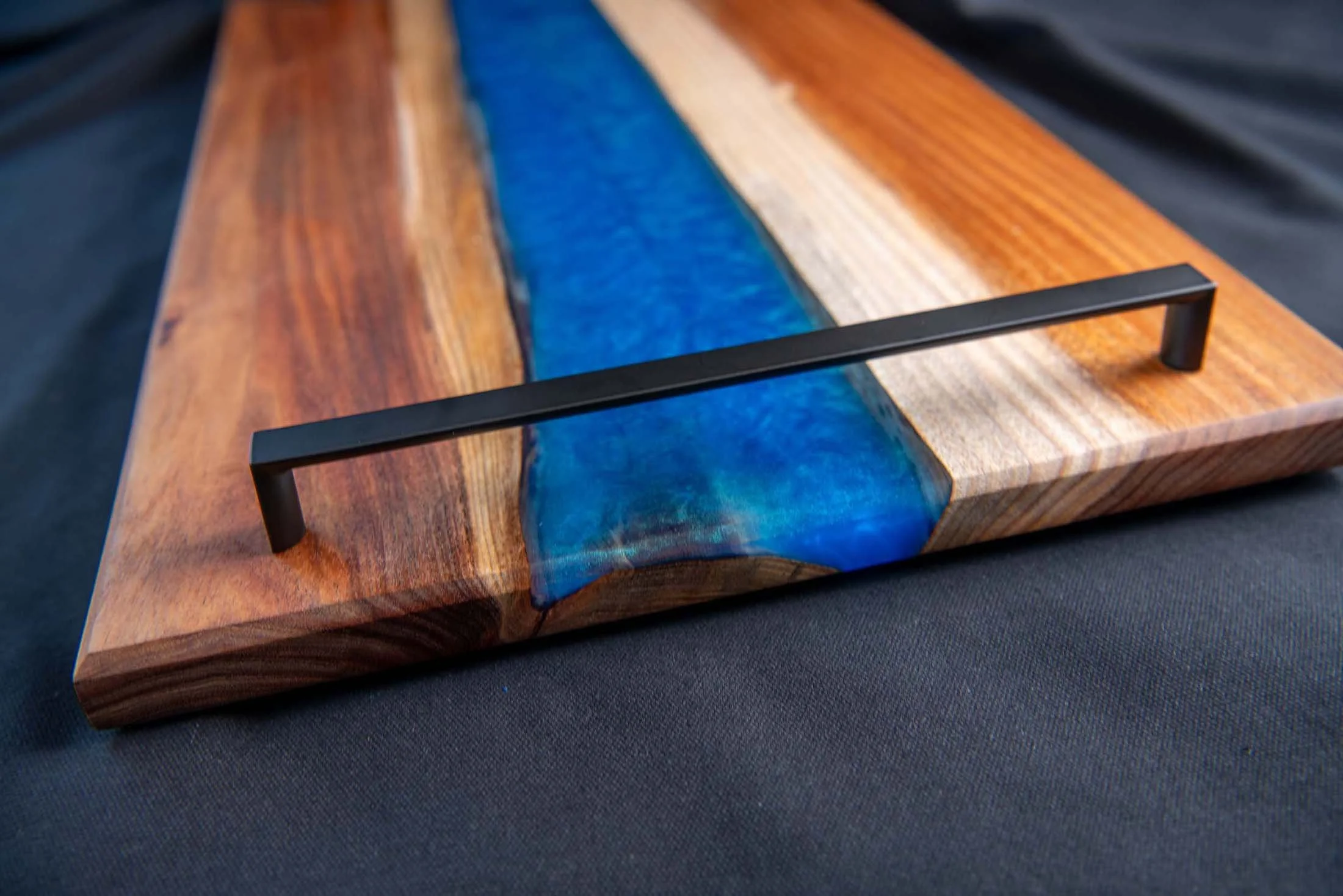 Blackwood charcuterie board with an Ocean Blue epoxy river and matt black handles.