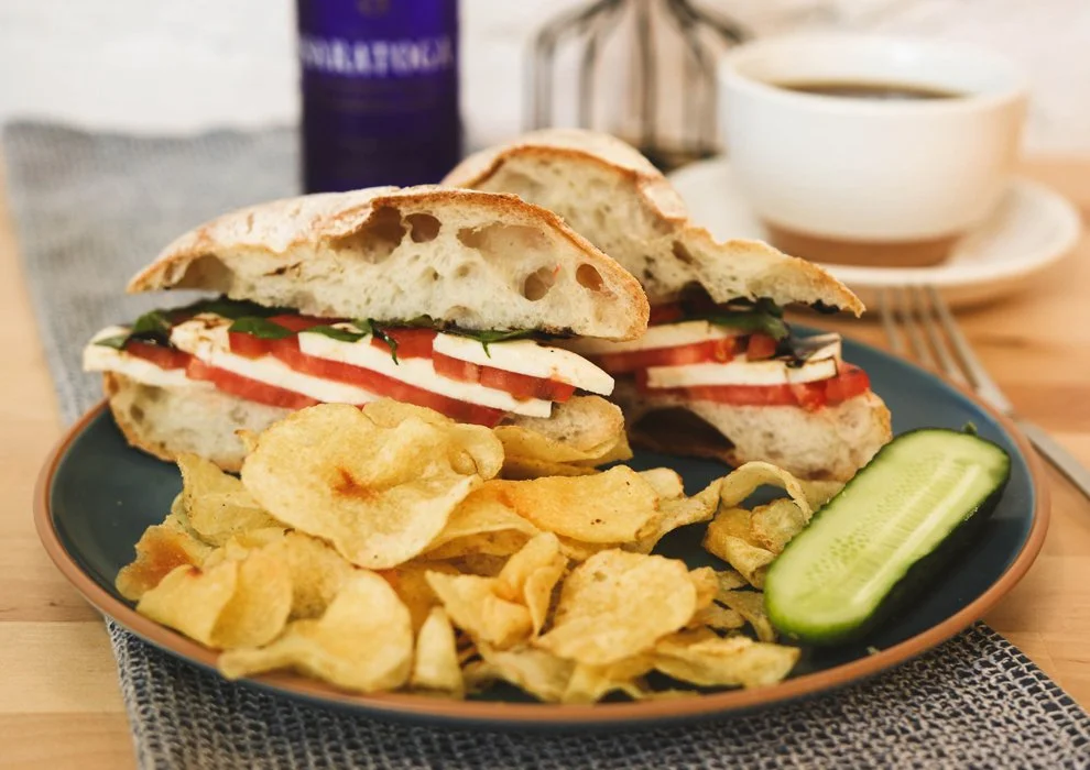 Classic Caprese. Ripe tomato, fresh mozzarella, basil leaves, extra virgin olive oil, balsami, on a plate with potato chips and a pickle.