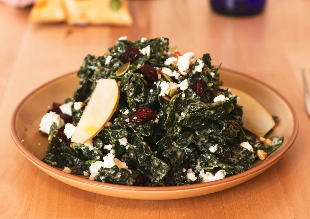 Kale Salad, Kale, goat cheese, dried cranberries, apple, toasted walnuts, pepitas, with lemon tahini dressing.