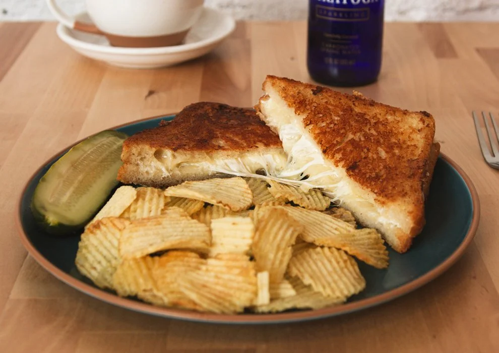 Zoller's Grown Up Grilled Cheese sandwich. Swiss and gruyere on sourdough, on a plate with potato chips and a pickle.