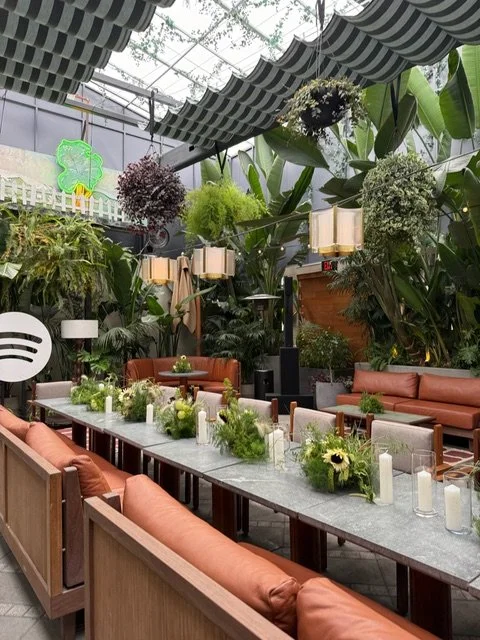 A woman in a white dress holding a large bouquet of various pastel-colored flowers, including pink orchids, orange carnations, and white roses, on a beach.