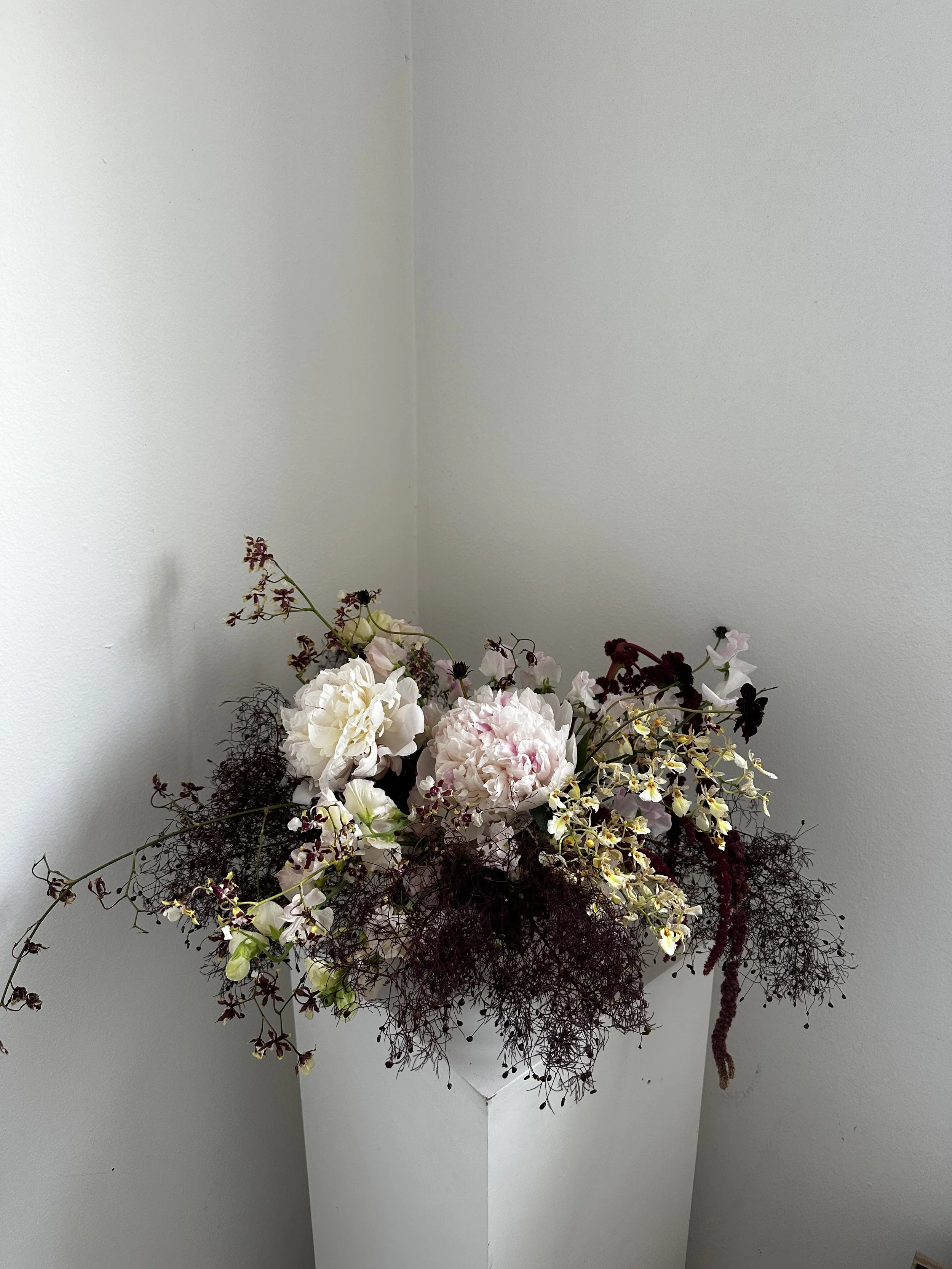 A bouquet of various flowers in a white vase against a plain white wall.