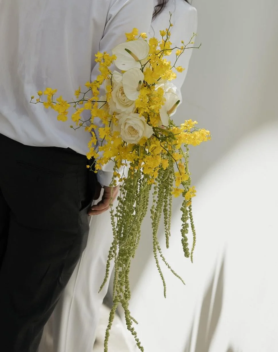 Person holding a cascading bouquet of white roses, yellow orchids, and green trailing plants.