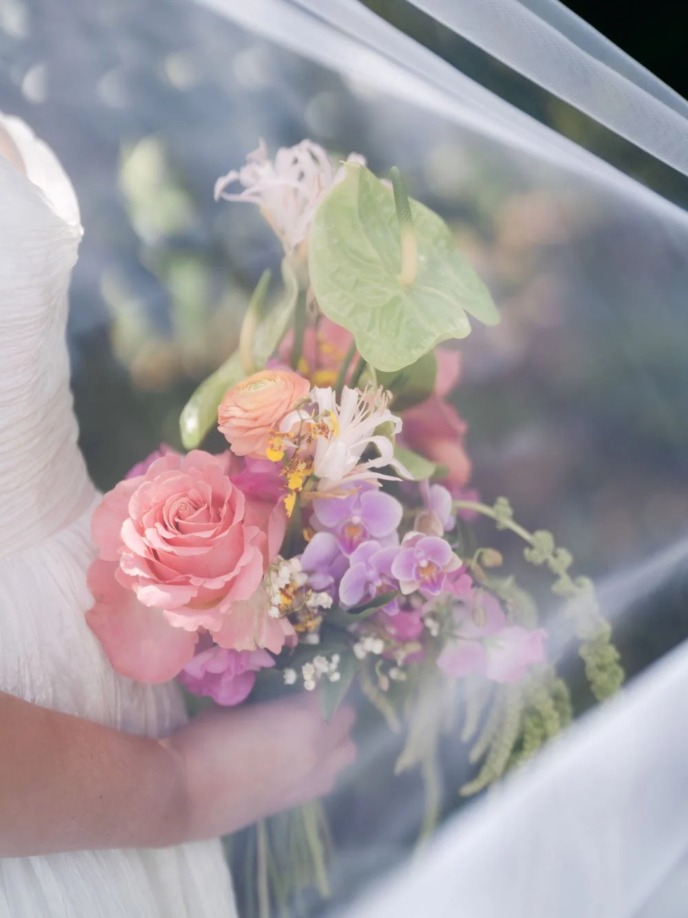 Close-up of a bouquet of soft pink, peach, and purple flowers viewed through a translucent veil or plastic cover.