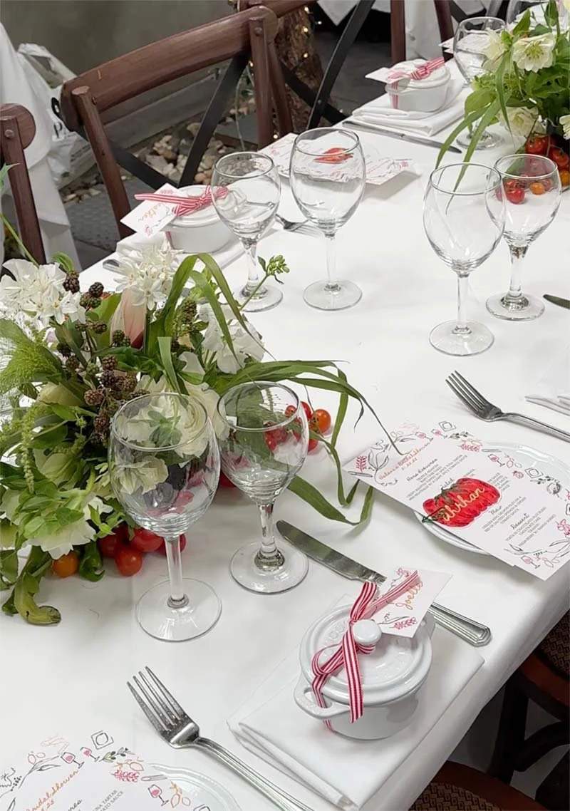 A decorated dining table with floral arrangements, wine glasses, utensils, and place cards for a celebration or event.