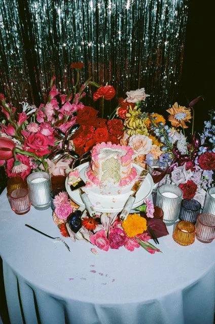 A decorated birthday cake on a table surrounded by colorful flowers and candles.