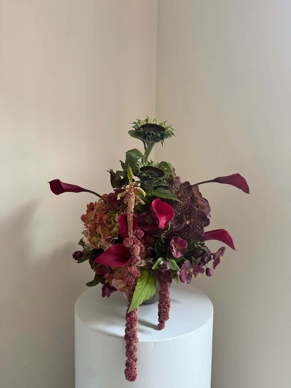 A floral arrangement with sunflowers, hydrangeas, and calla lilies in a vase on a white stand.