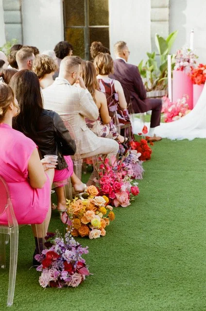 People seated at a wedding ceremony, decorated with pink and orange flowers.