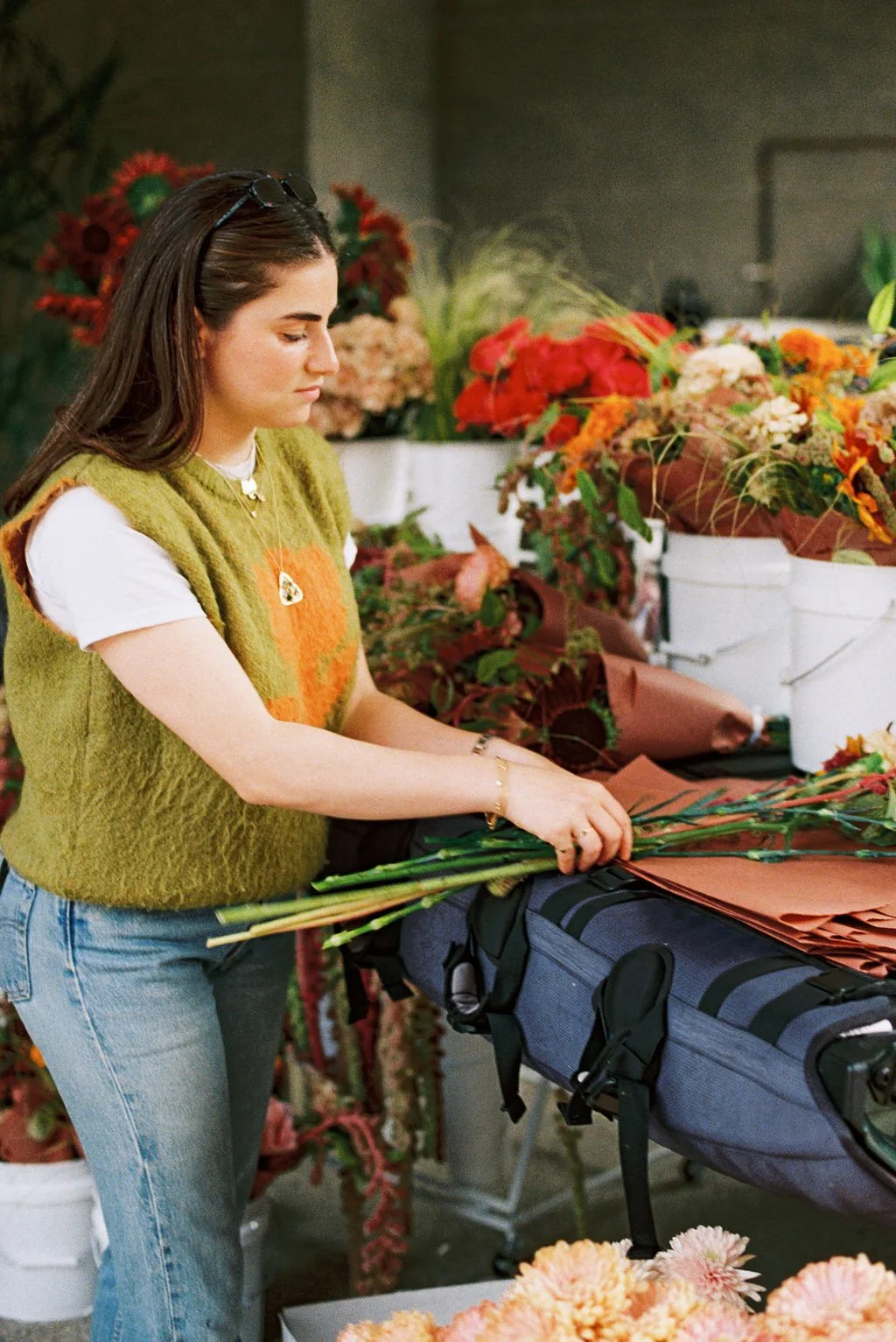 A woman arranging flowers at a flower shop with various colorful floral arrangements in buckets behind her.