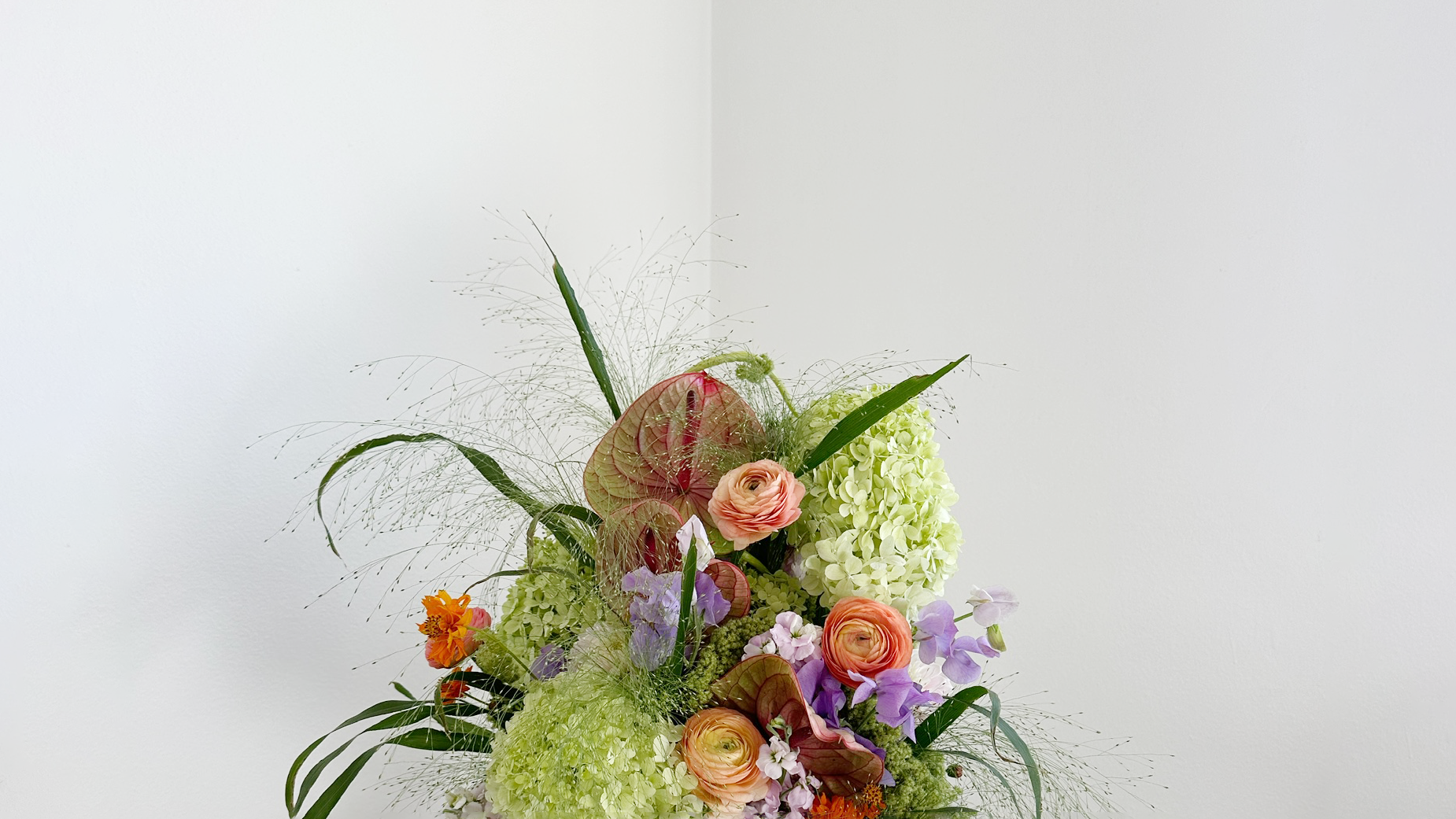 A floral arrangement with pink and orange roses, green and white hydrangeas, purple and violet flowers, and greenery against a white background.