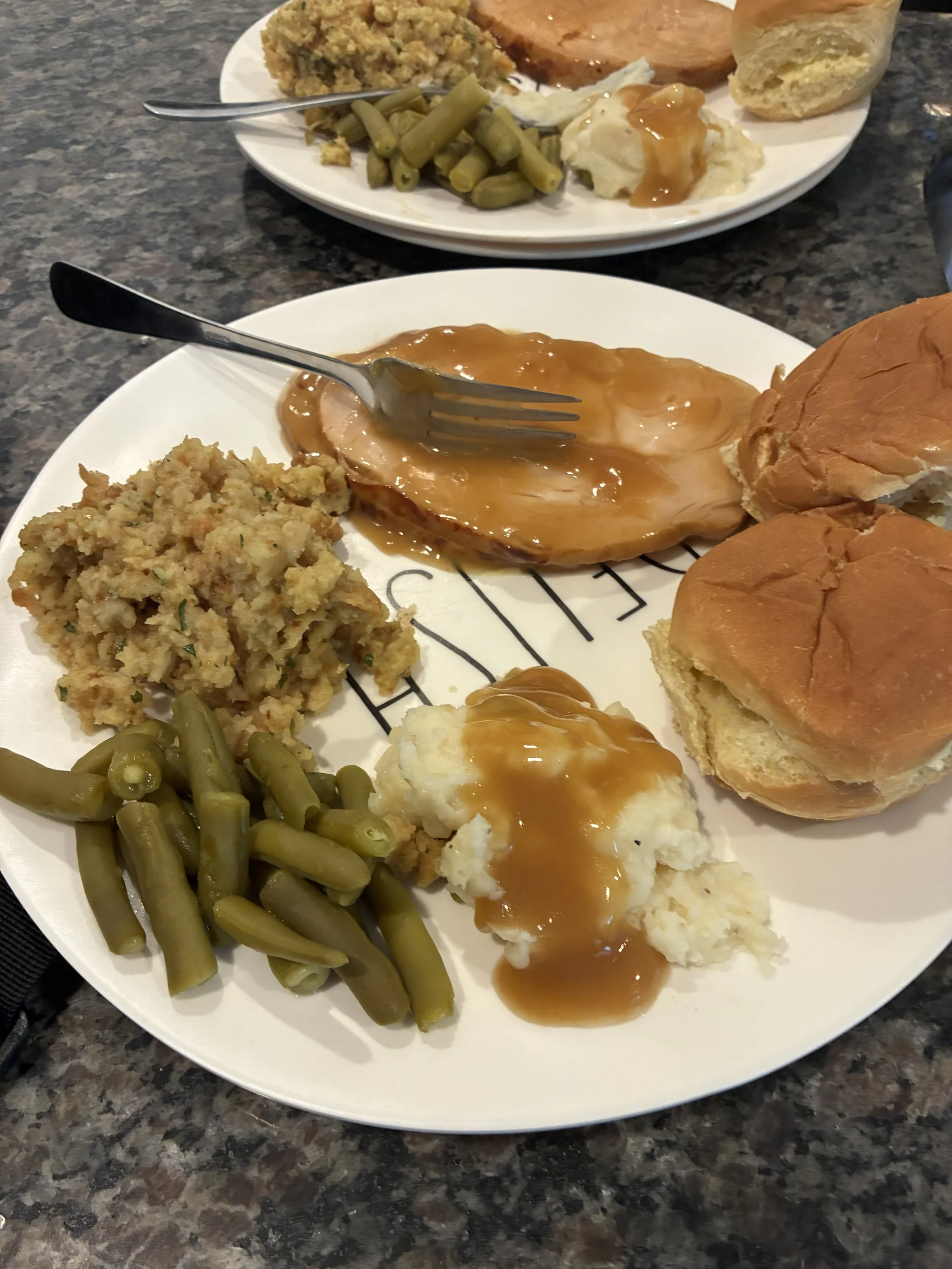 A full plate of food for Thanksgiving with turkey, stuffing, rolls, green beans, and mashed potatoes