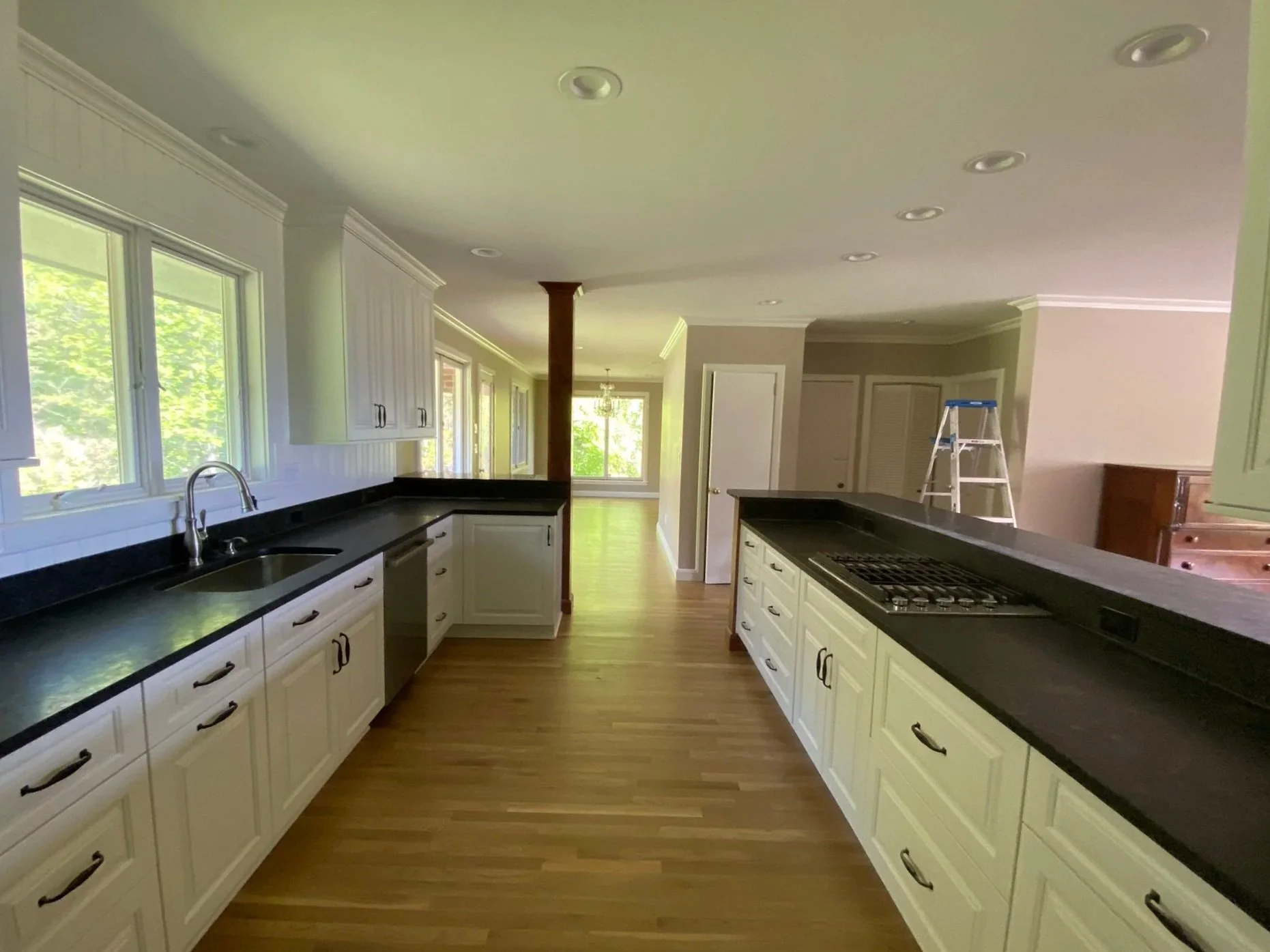 Modern kitchen remodel in Asheville, NC, featuring a spacious galley layout with white shaker cabinets, dark soapstone countertops, stainless steel appliances, and refinished light oak hardwood floors.
