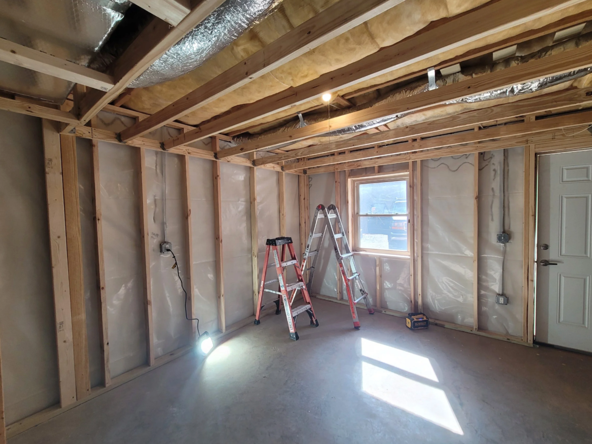 Interior view of a professional basement finishing project in Asheville, NC, showing new wood stud framing, vapor barrier installation, and ceiling insulation for a moisture-controlled living space.