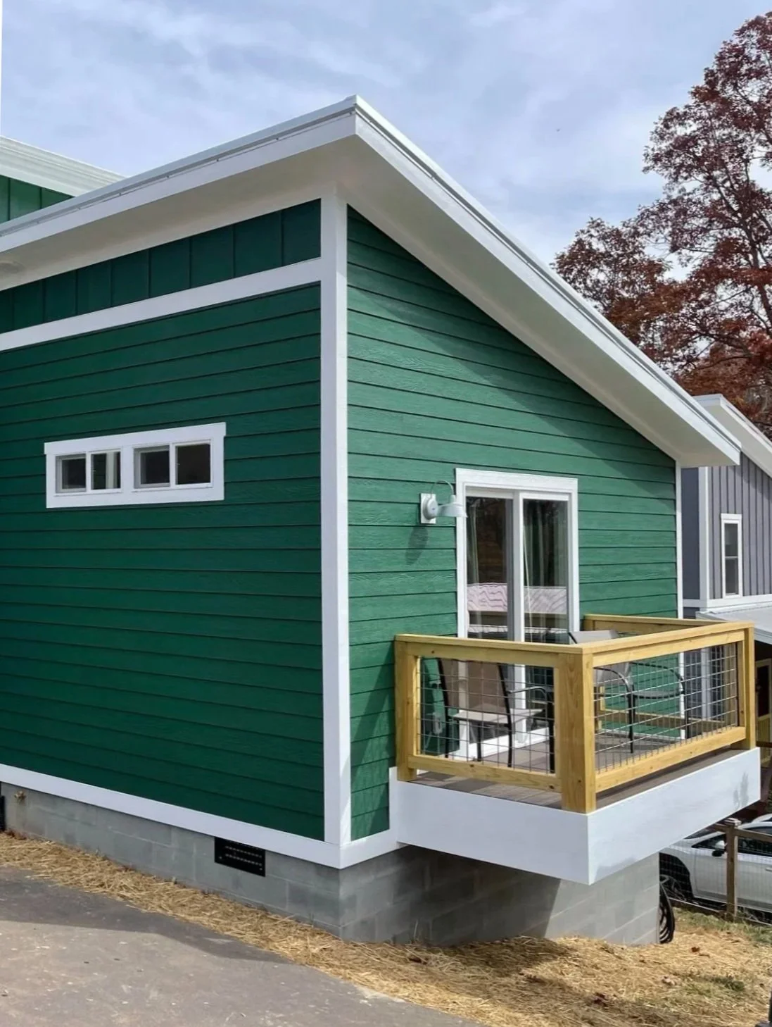 Modern master bedroom and bathroom home addition in Asheville, NC, featuring forest green lap siding, white trim, and a private cantilevered balcony with a custom wood and wire mesh railing.