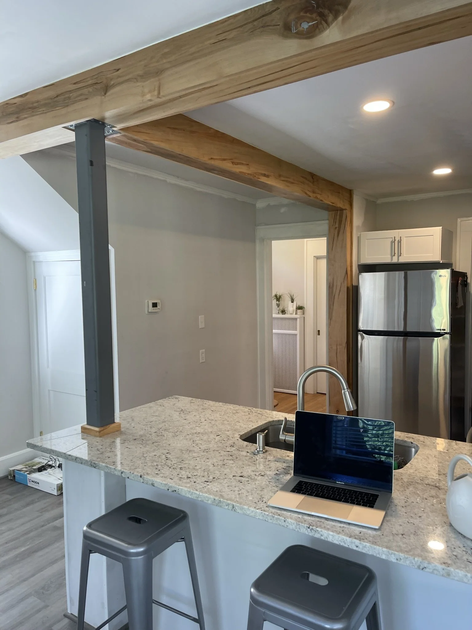 After photo of a structural renovation in West Asheville showing a finished open concept kitchen. A load-bearing LVL beam is professionally wrapped in natural wood, supported by a sleek charcoal gray steel post, opening up the kitchen to the living a