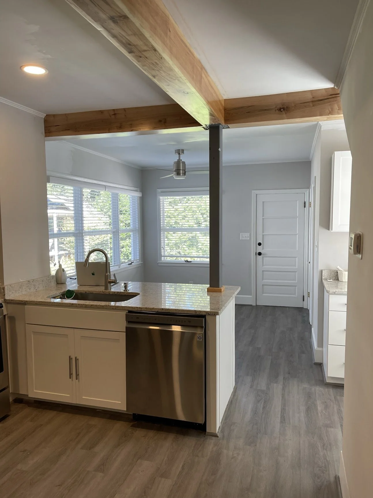 After photo of a structural renovation in West Asheville showing a finished open concept kitchen. A load-bearing LVL beam is professionally wrapped in natural wood, supported by a sleek charcoal gray steel post, opening up the kitchen to the living a