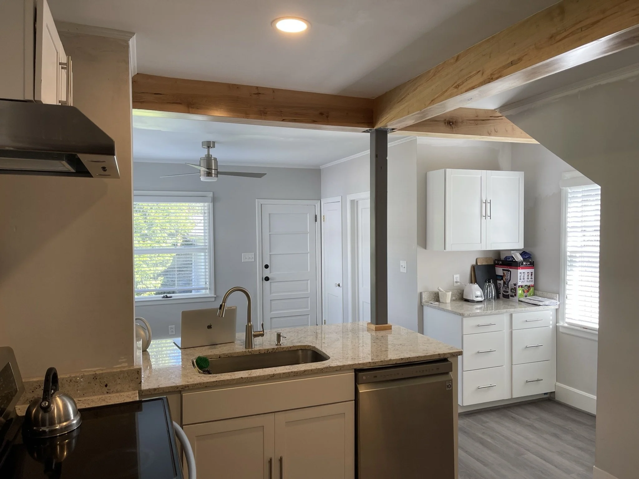 After photo of a structural renovation in West Asheville showing a finished open concept kitchen. A load-bearing LVL beam is professionally wrapped in natural wood, supported by a sleek charcoal gray steel post, opening up the kitchen to the living a