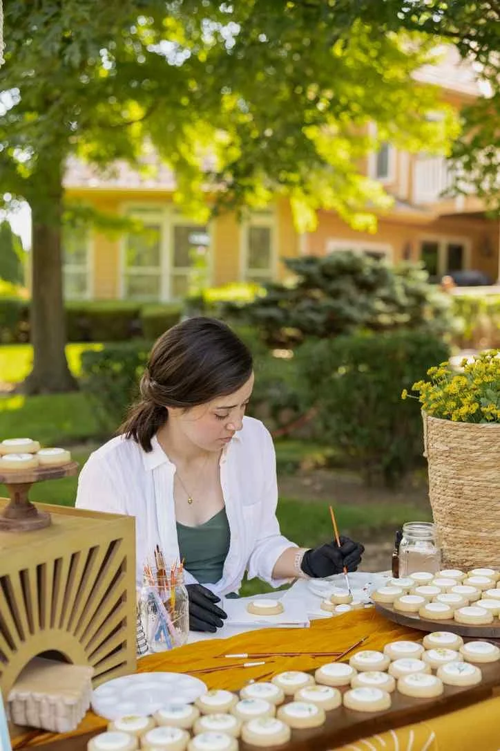A Cookie Artist is painting floral designs on cookies at a baby shower.