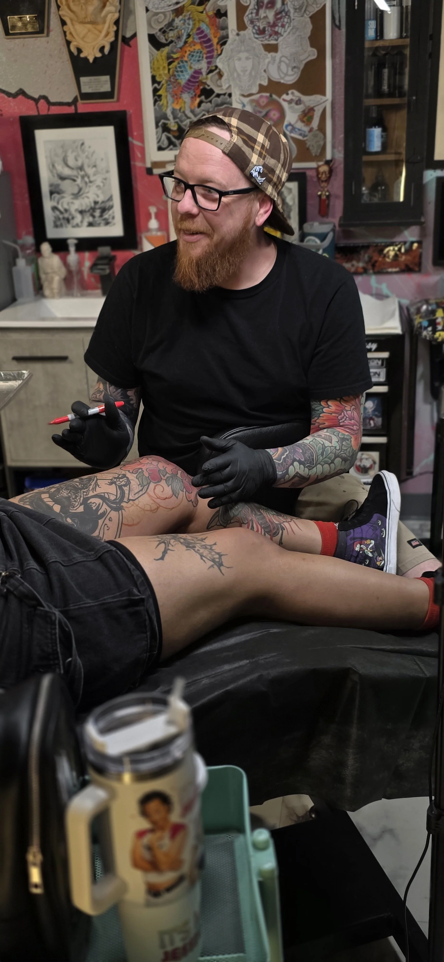 Japanese Tattoo Artist drawing on tattoo design to client's leg