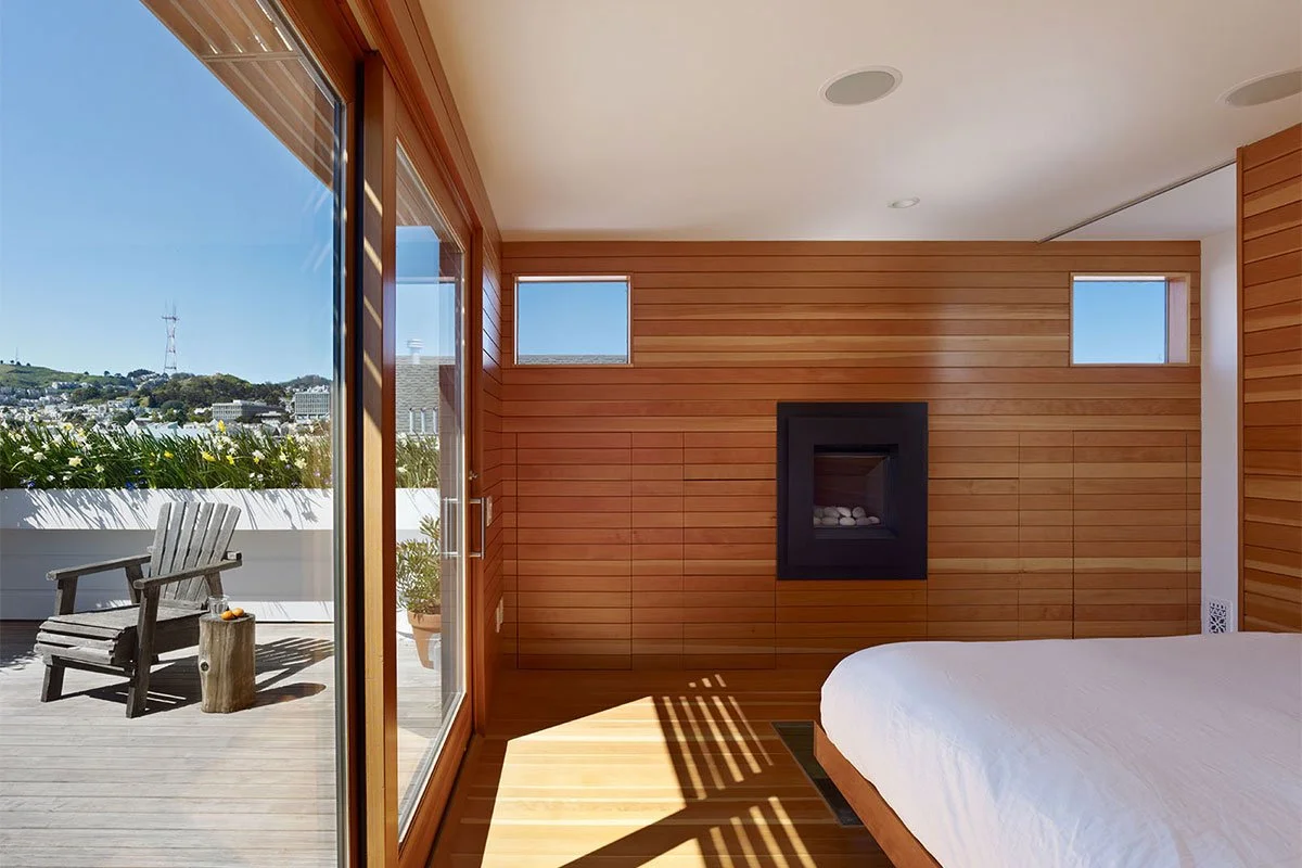 A serene bedroom lined with rich wood paneling, with sliding glass doors leading to an outdoor space, including a built-in fireplace for added warmth.