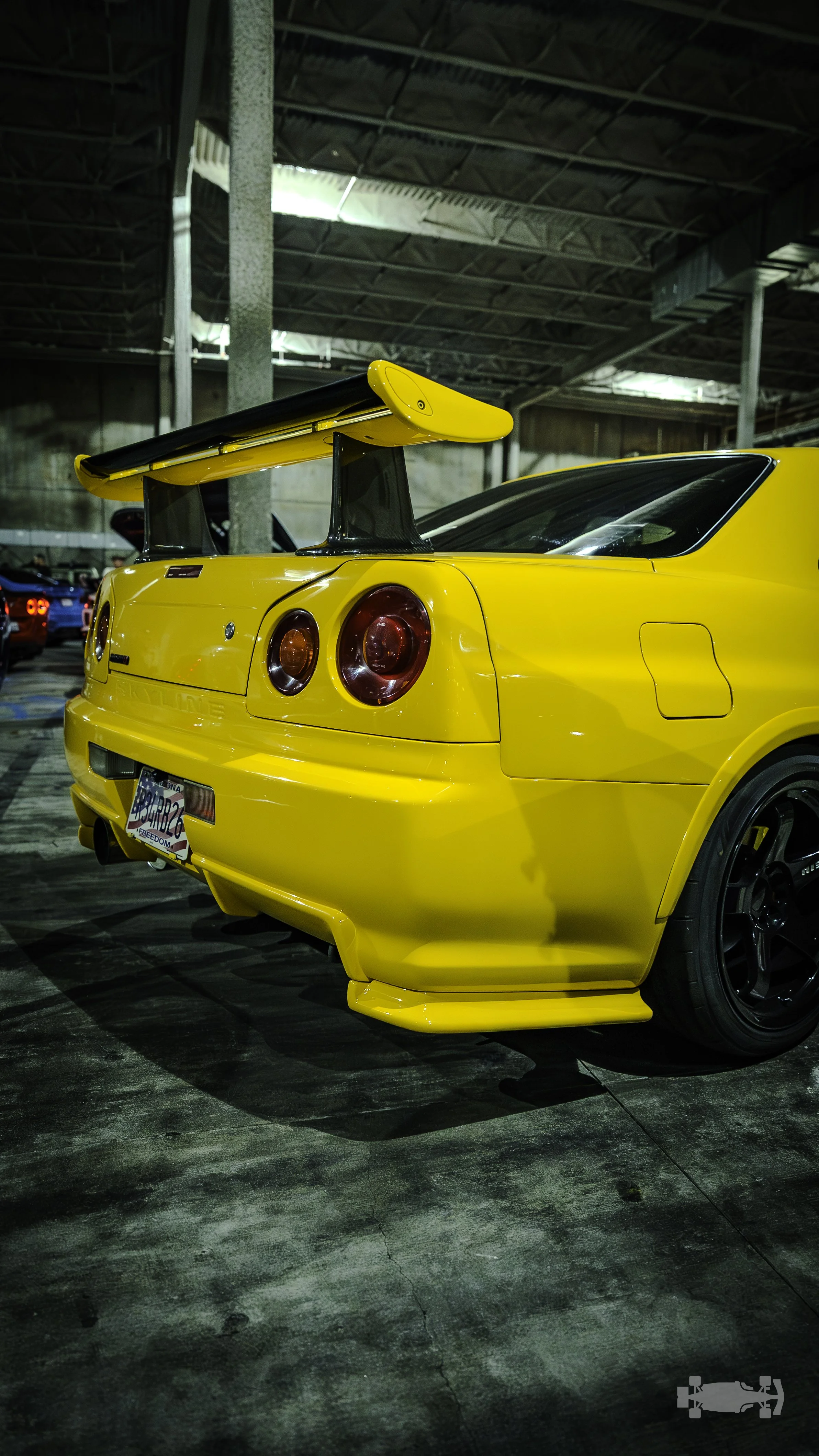Yellow sports car with large rear wing spoiler parked indoors.