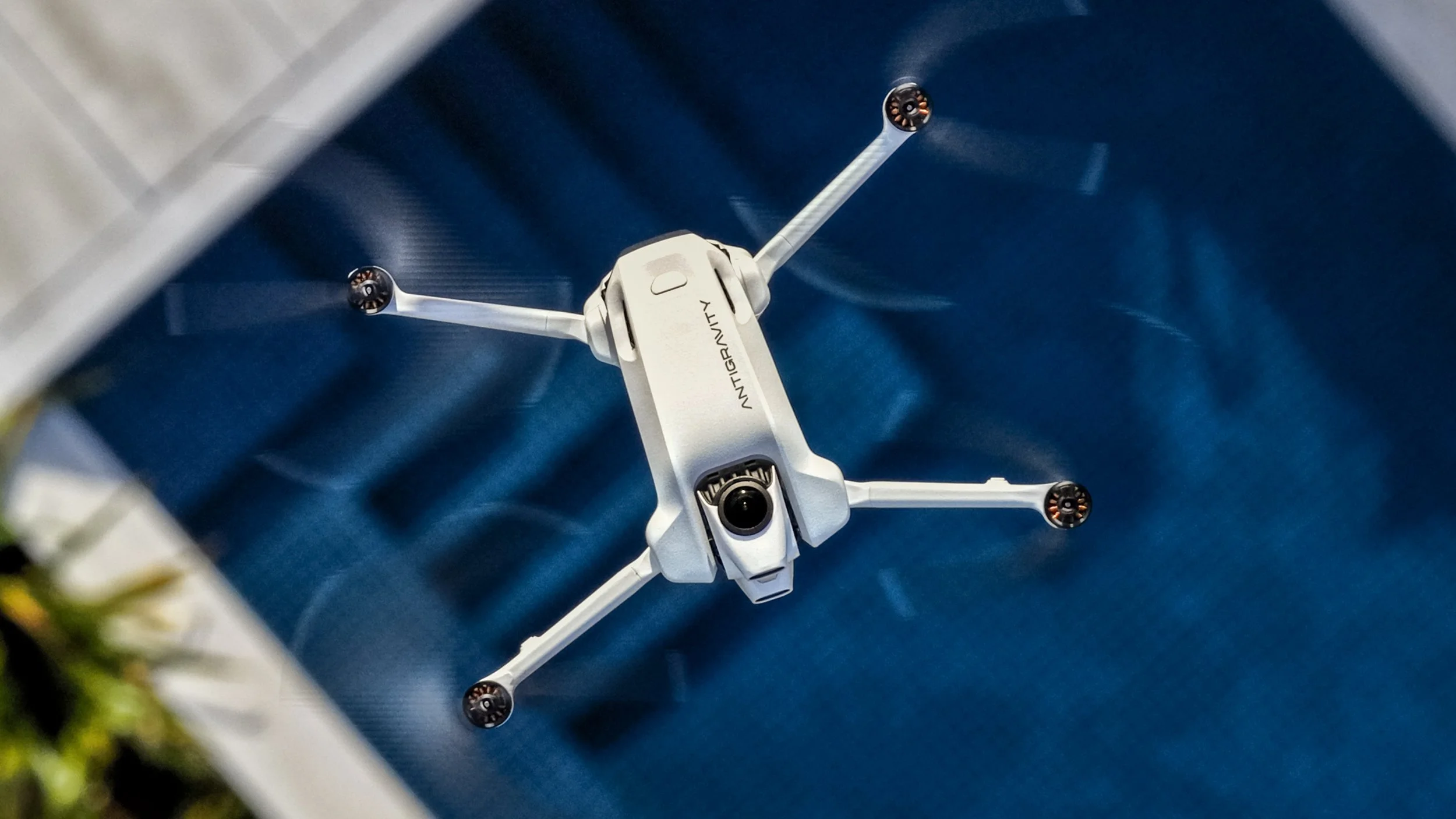 A white DJI Mavic Mini drone with four propellers takes off from a blue surface, viewed from above.