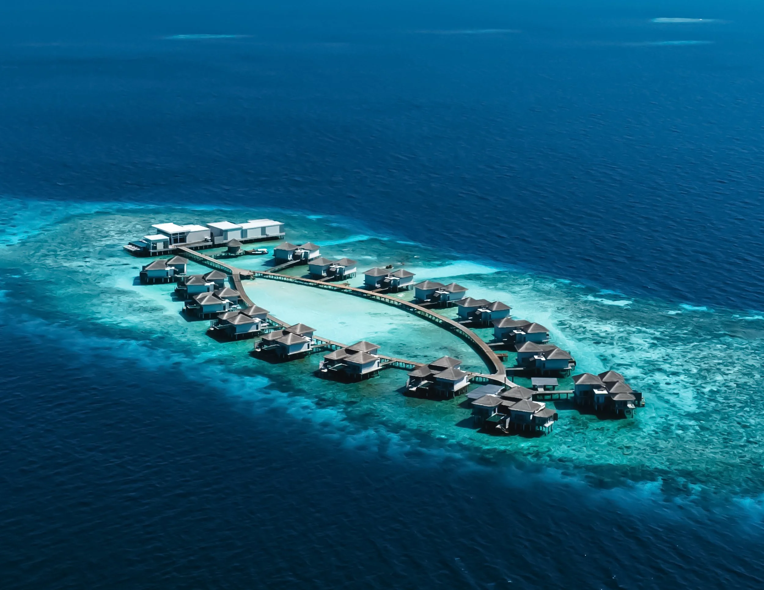 Aerial view of overwater bungalows on a tropical island, surrounded by clear blue water.