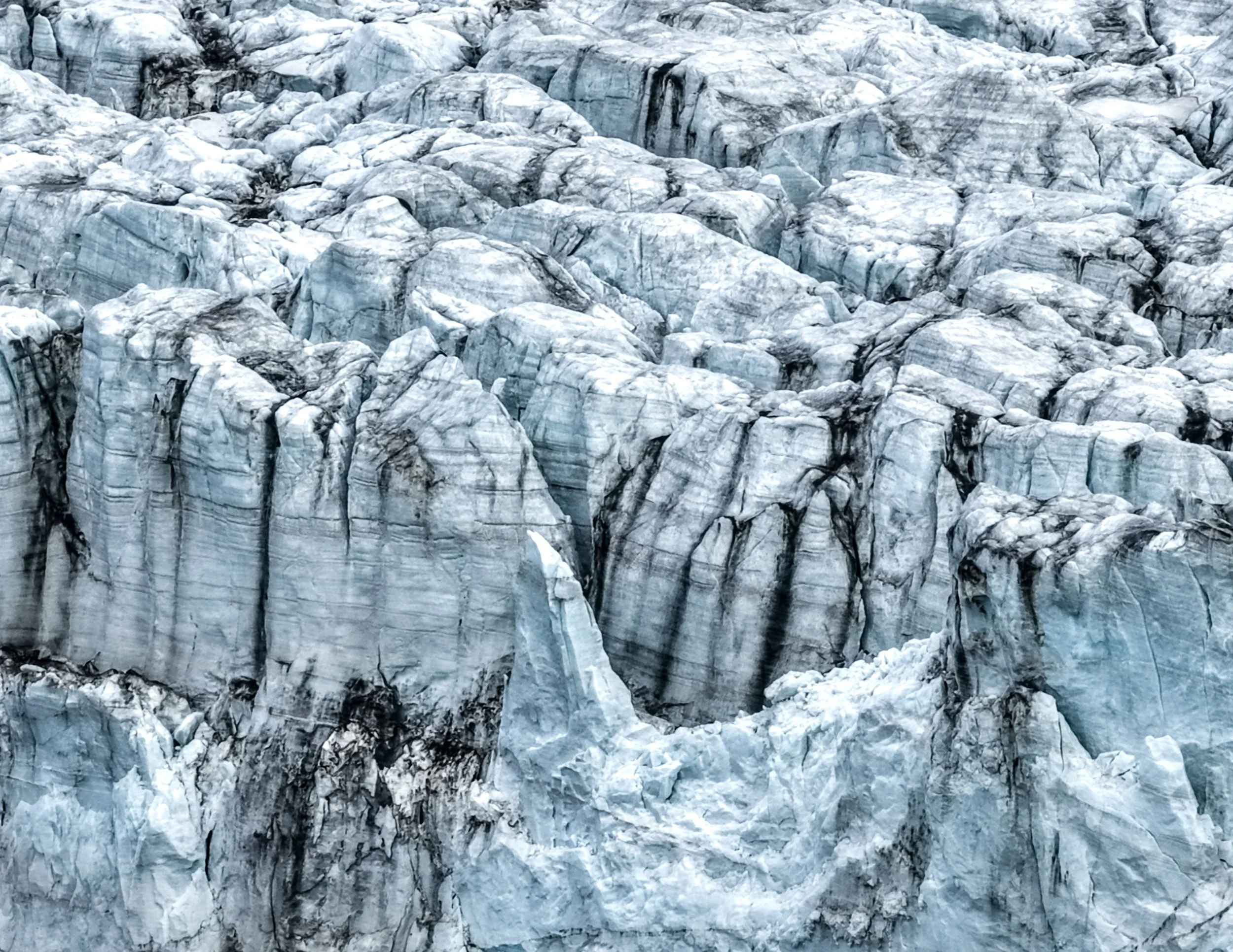 Close-up view of a glacier with large chunks of ice and visible crevasses, showing layers of ice with shades of white and blue.
