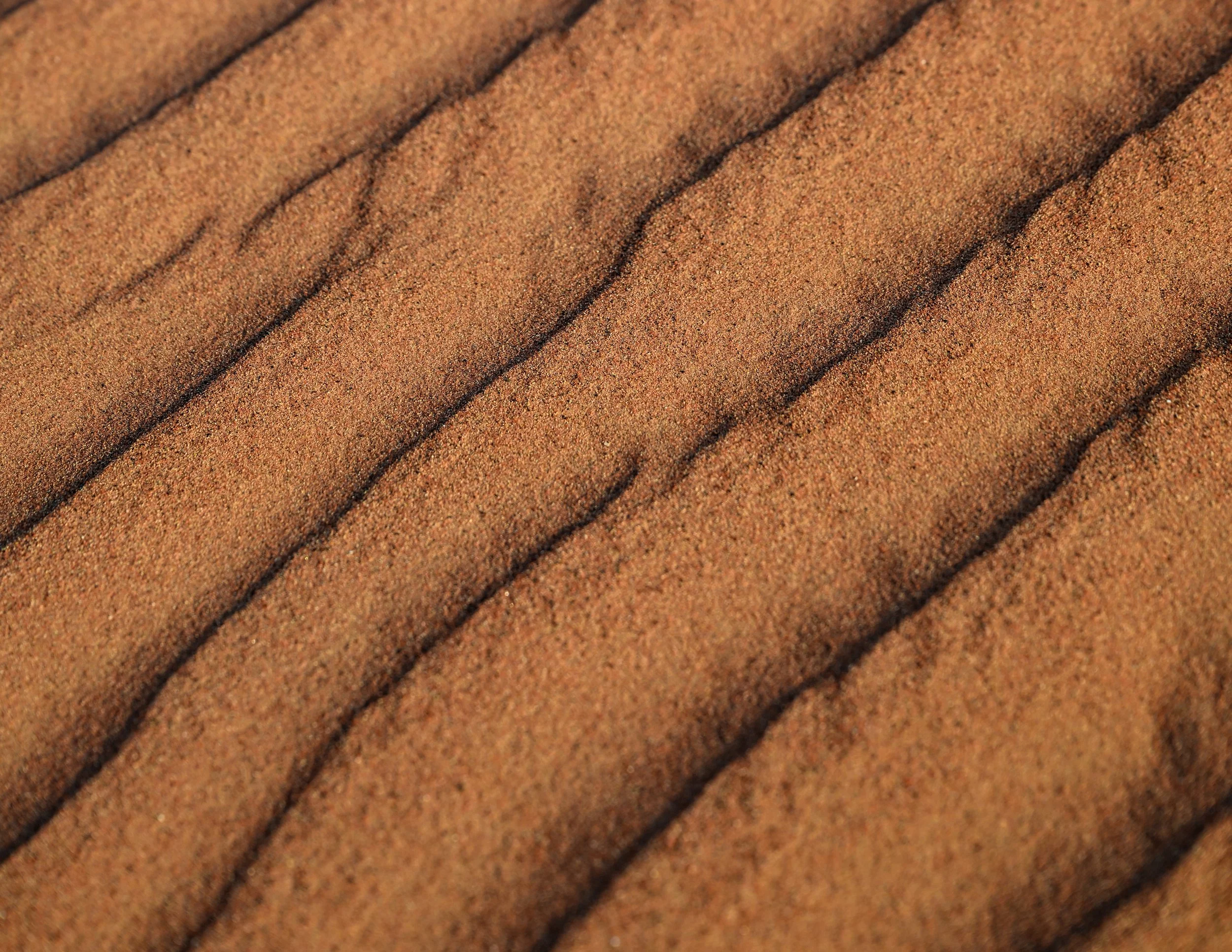 Close-up view of textured desert sand with evenly spaced, parallel ridges.