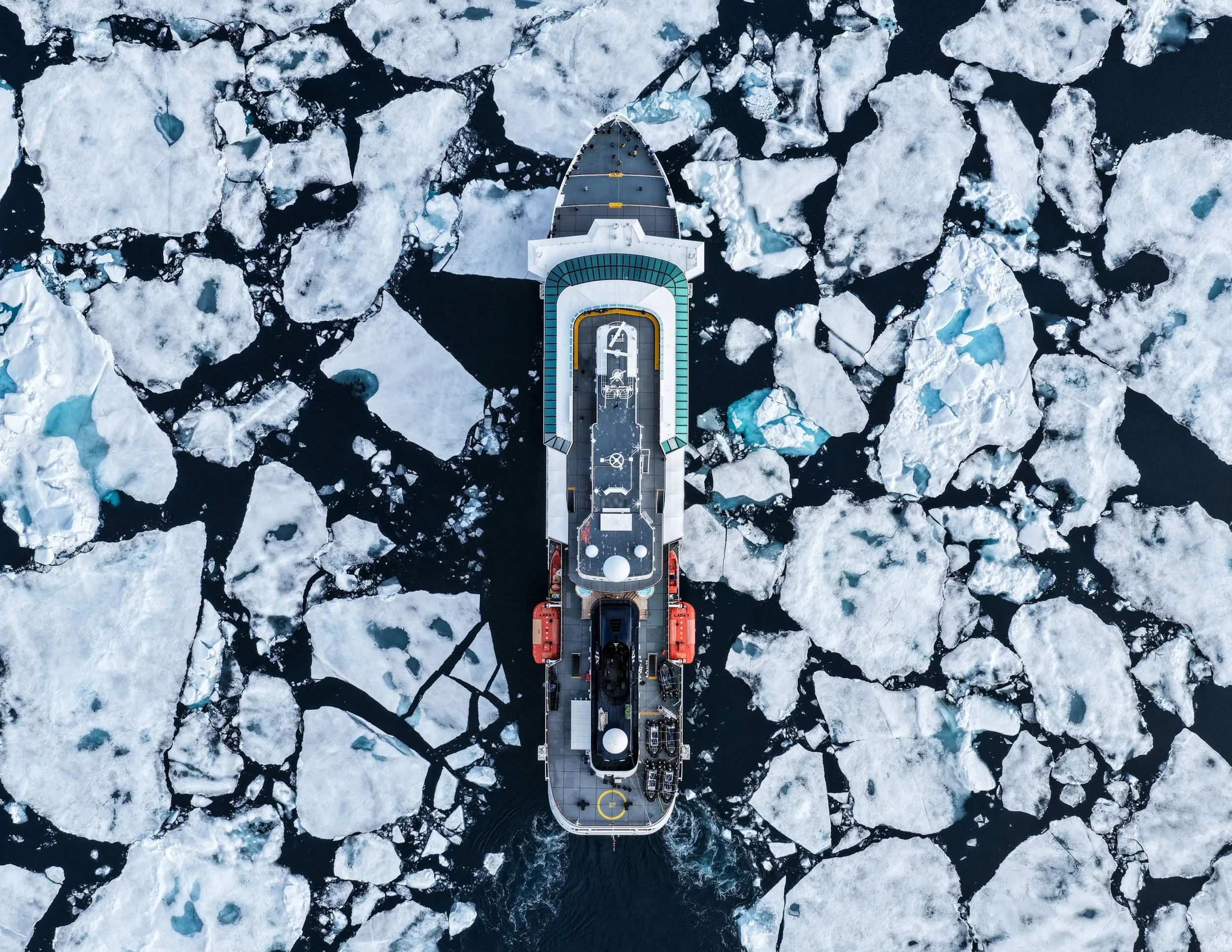 An aerial view of a ship navigating through icy waters with floating icebergs and sea ice.