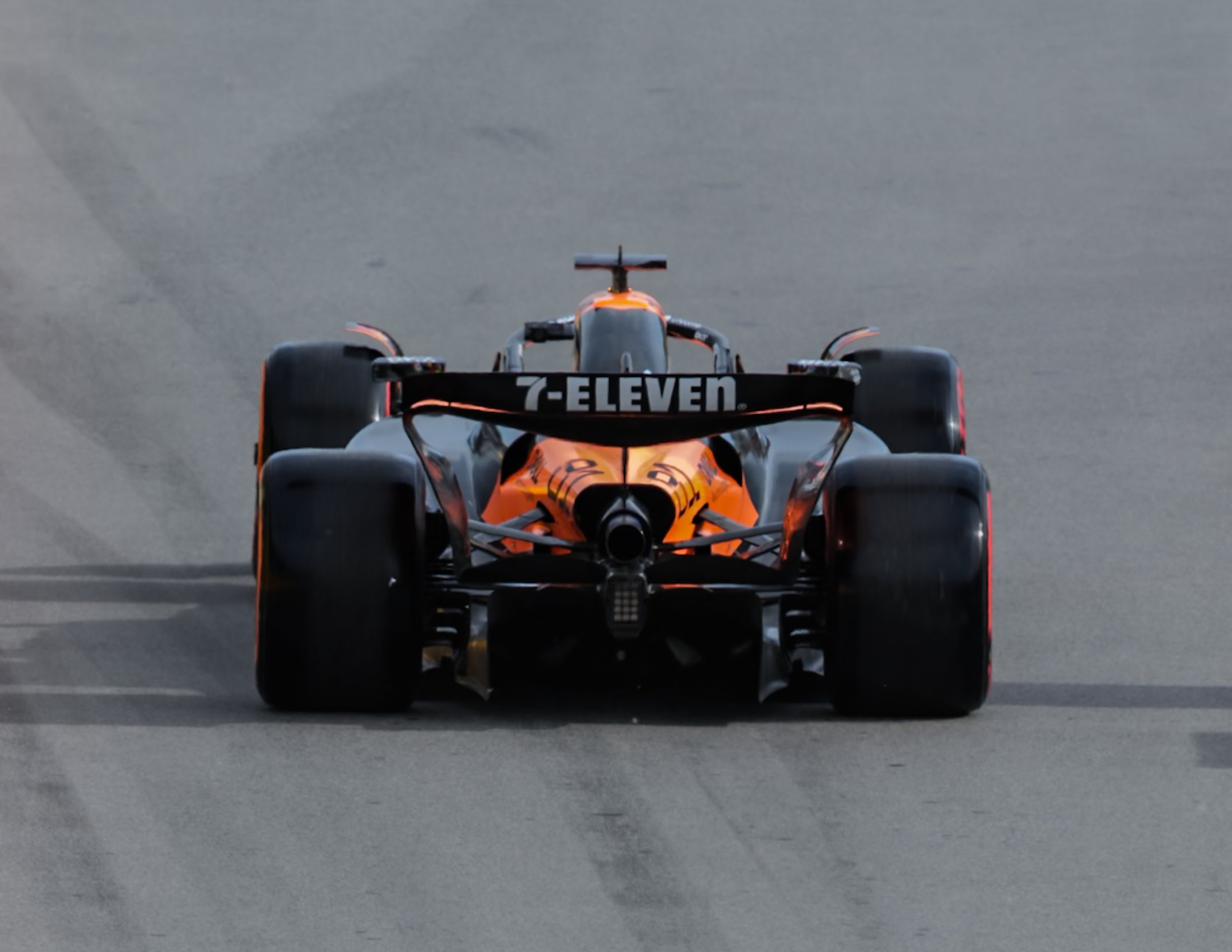 Race car on a track with an orange and black color scheme, featuring sponsorship logos, viewed from the front.