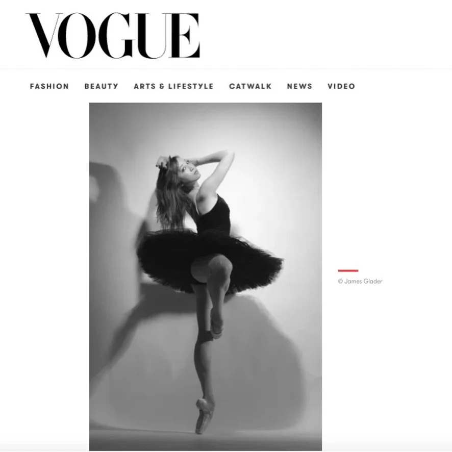 Black and white photo of Merritt Moore a ballet dancer in a tutu and pointe shoes balancing on one leg with one arm raised and the other behind her head against a plain background for Vogue.