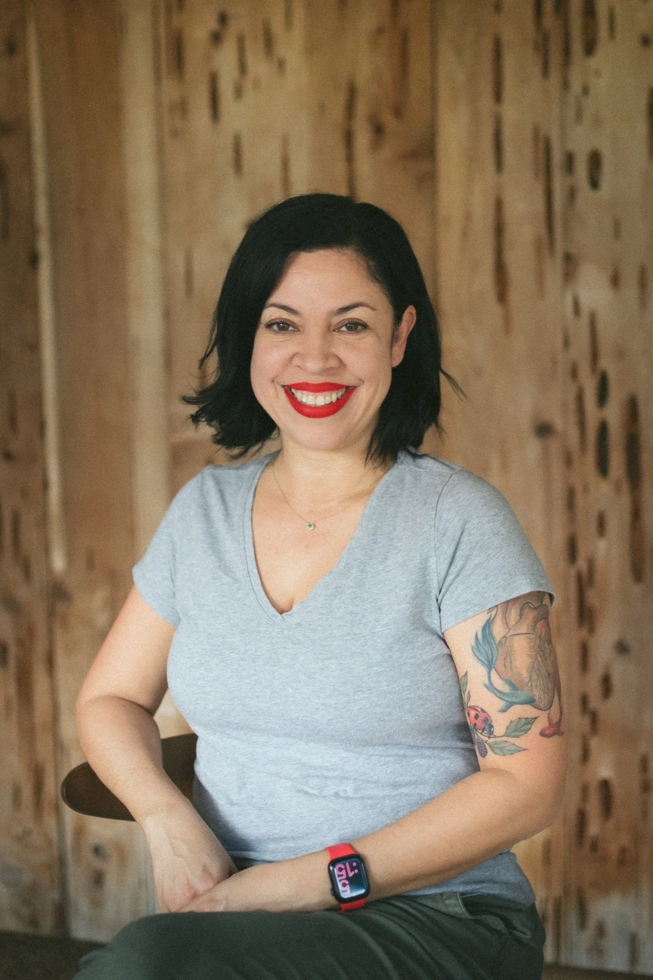 Portrait of artist Jacqueline Bermudez smiling in a gray t-shirt with a heart tattoo on her arm