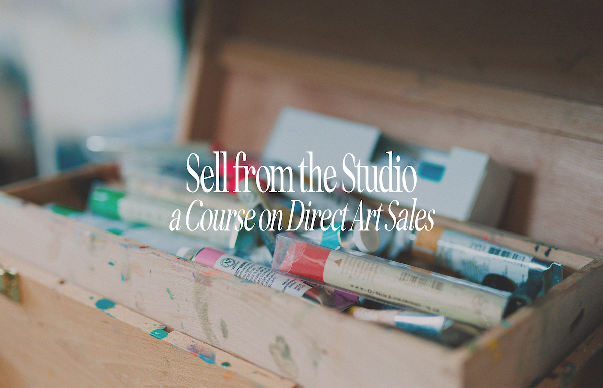 Open wooden art supply box with various tubes of paint and art supplies inside, sitting on a wooden surface.