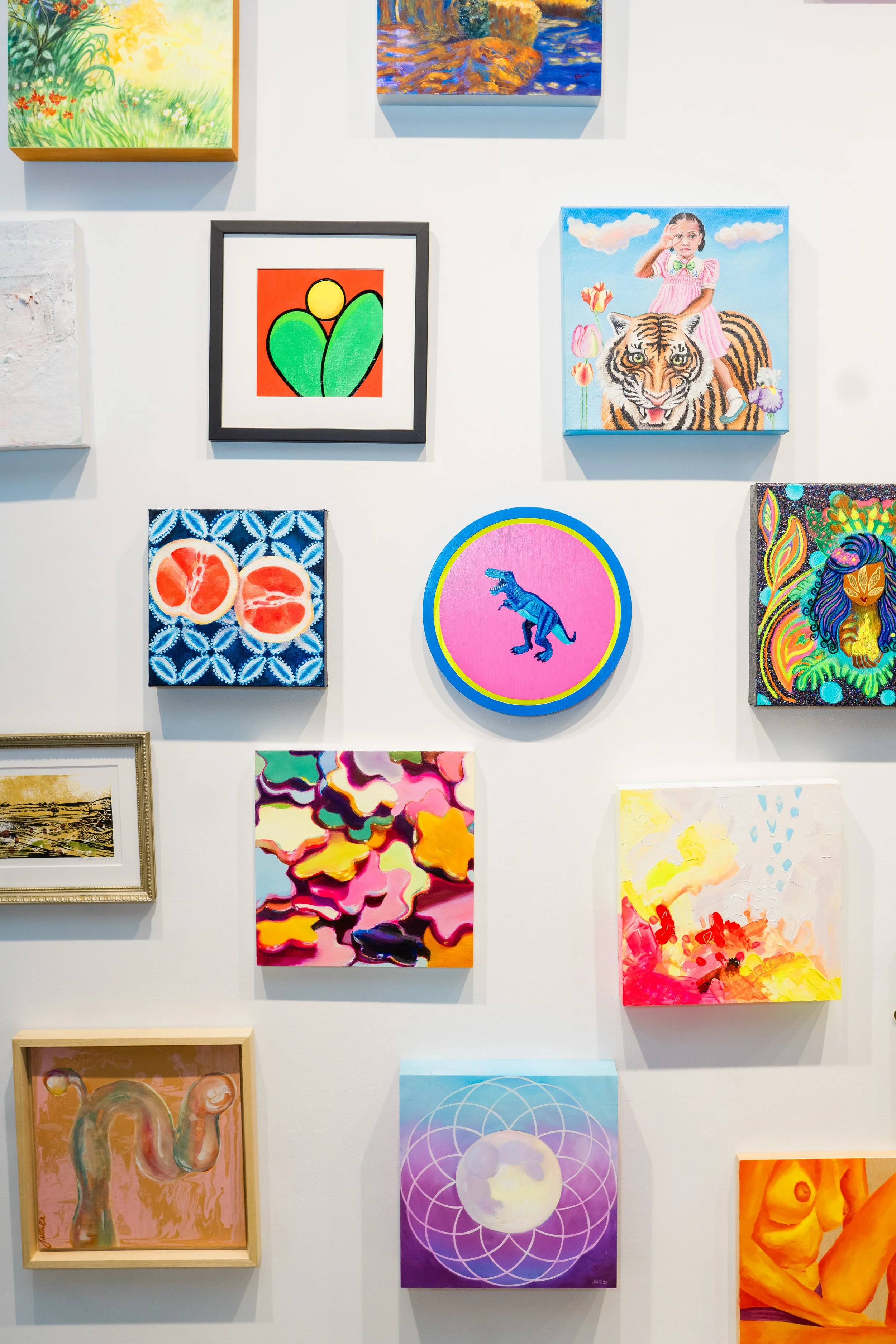 A wall with multiple colorful paintings, including a girl riding a tiger, a dinosaur, an abstract floral, a face, and various other abstract and nature-themed artworks.