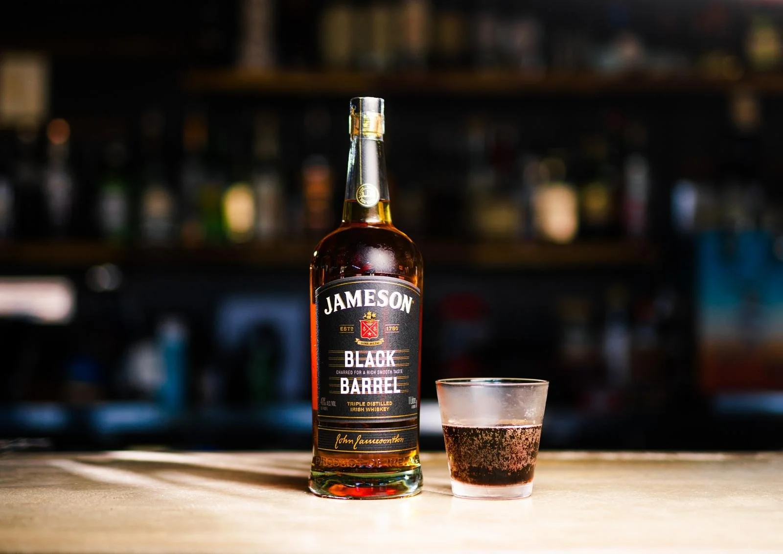A bottle of Jameson Black Barrel Irish whiskey and a glass with whiskey on a bar counter.