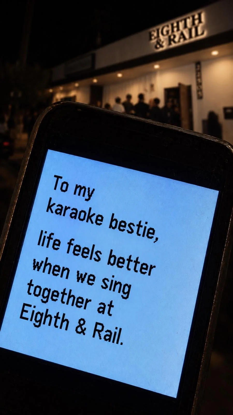 A phone screen displaying a message to a karaoke friend, with a building labeled 'Eighth & Rail' in the background at night.