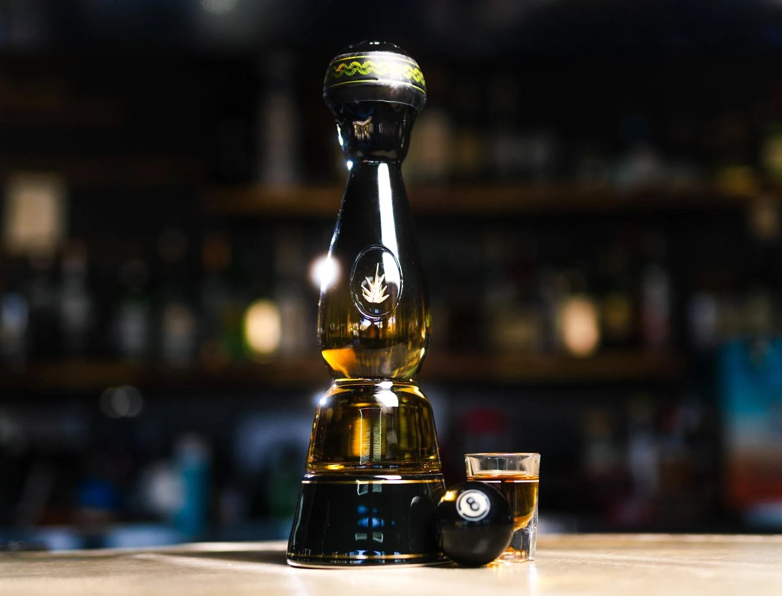 A game of pool with a glass of whiskey and a black eight ball on a wooden table.