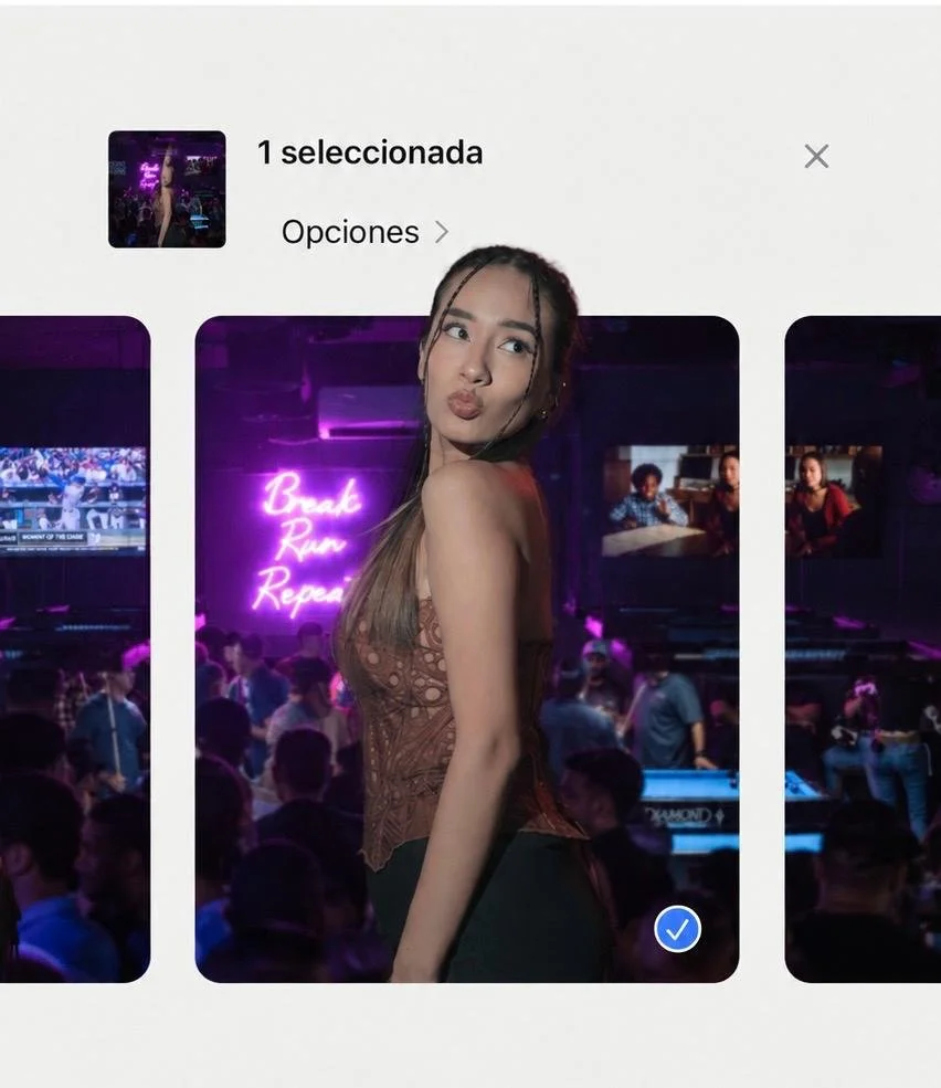 A young woman with long hair and a sleeveless top making a pouty face inside a dimly lit venue with pink neon signs and people in the background.