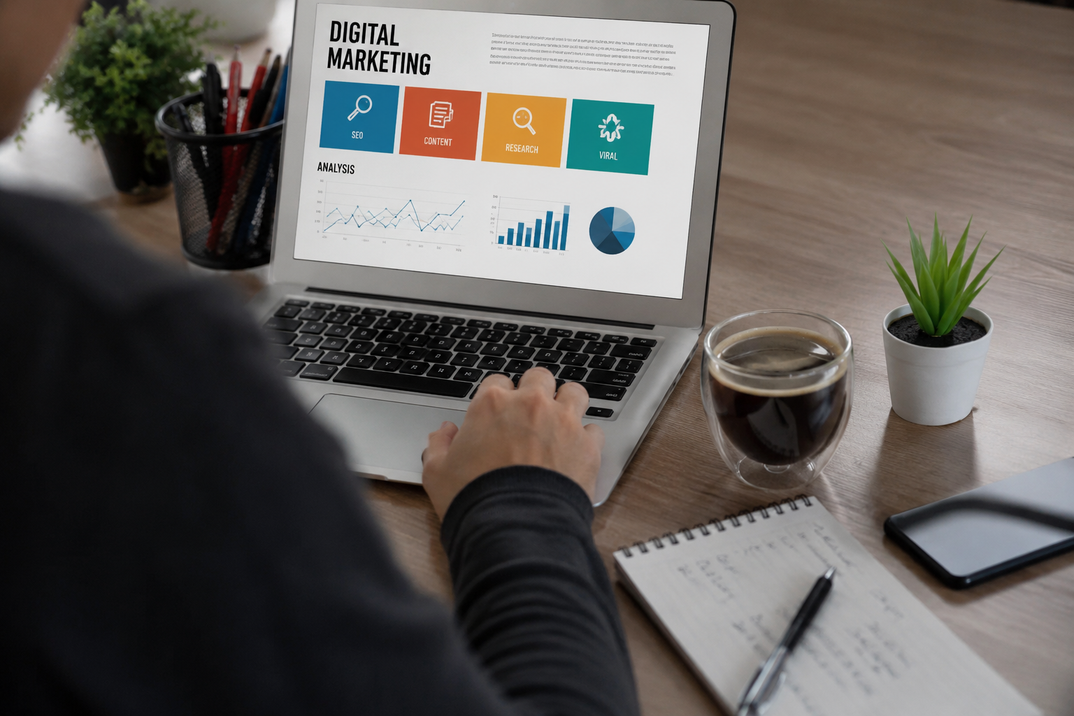 Laptop displaying a digital marketing presentation with analysis charts and icons for SEO, content, research, and viral marketing, on a wooden desk with notepad, pen, coffee, plant, and smartphone.