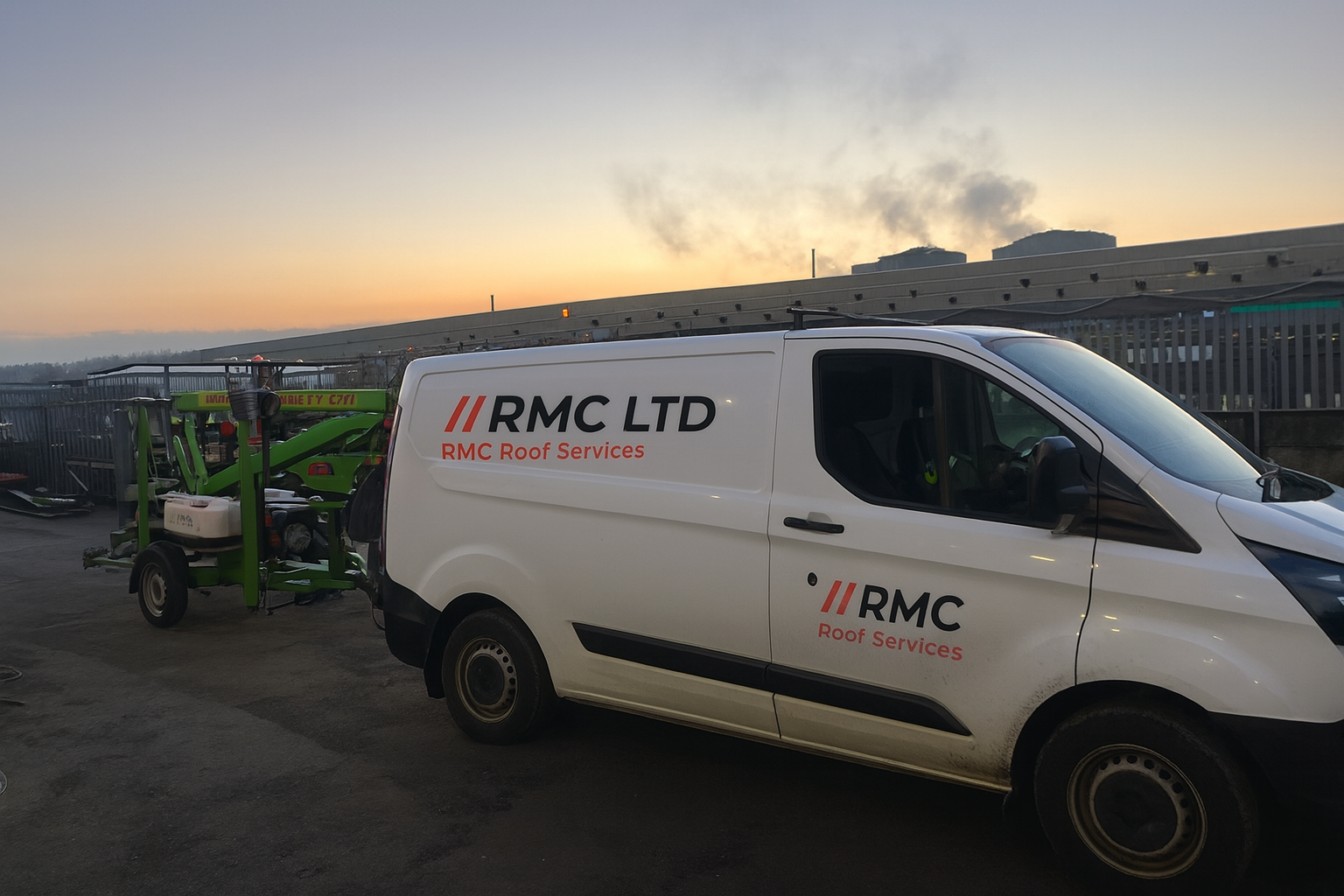 A white van with the logo 'RMC LTD RMC Roof Services' parked outdoors at sunset, attached to green roofing equipment, with a background of a rooftop and distant industrial buildings emitting smoke.