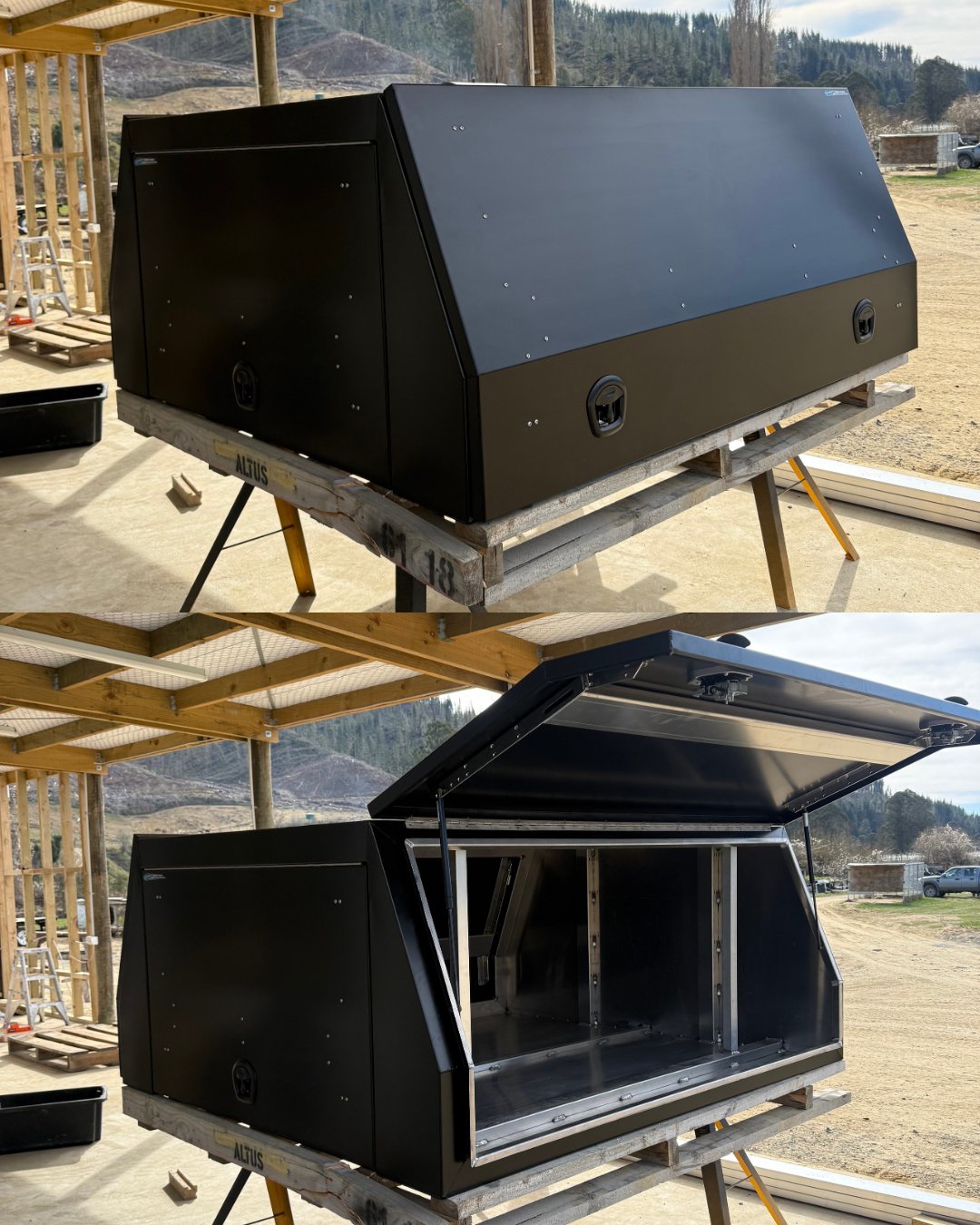 Two photos of a black metal storage enclosure. The top photo shows it closed, side view. The bottom photo shows it open, with a hydraulic lift mechanism holding the lid up. The structure is outdoors on wooden workbenches with a rural landscape in the